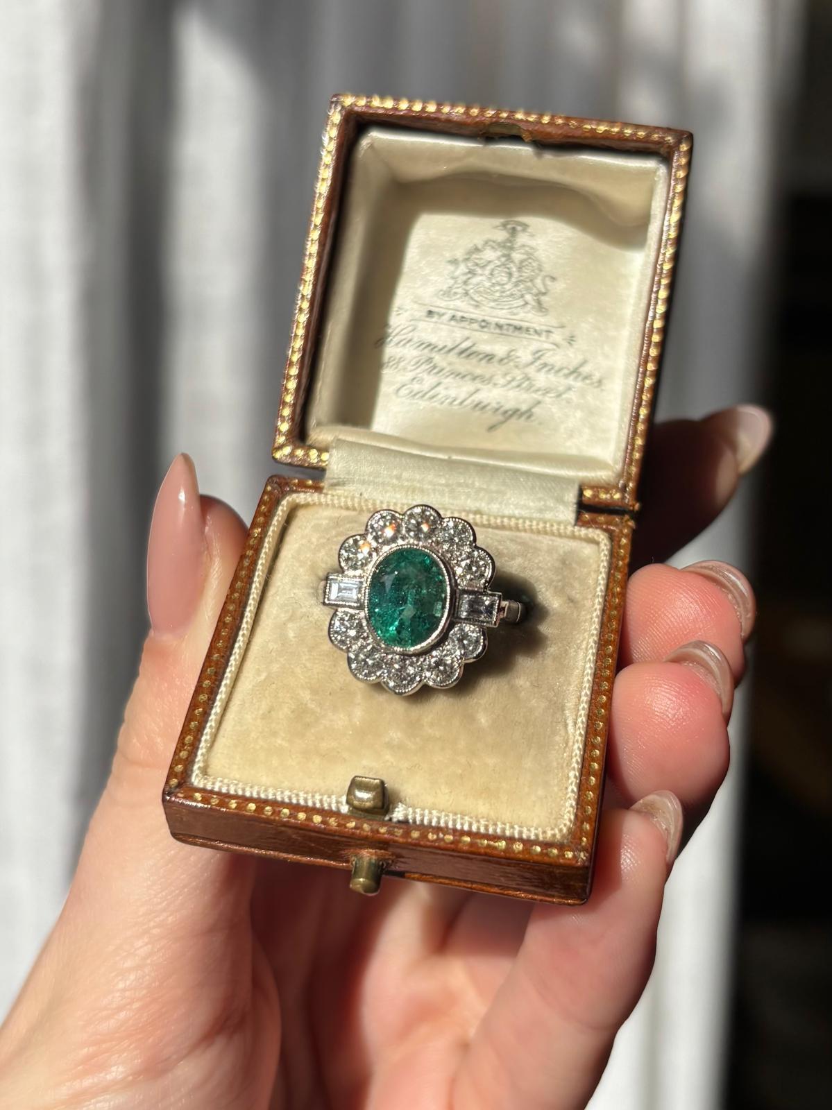 Magnifique bague vintage en platine sertie d'émeraudes et de diamants. 

La bague est sertie d'une vibrante émeraude de taille ovale qui est solidement sertie par frottement au centre dans un subtil sertissage à mille grains.  L'émeraude est