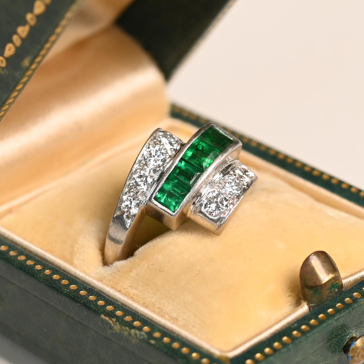 Dieser exquisite Ring aus der Retro-Ära zeigt ein auffälliges geometrisches Design, das um 1940 in sorgfältiger Handarbeit aus Platin gefertigt wurde. In der Mitte ist eine Reihe leuchtender Smaragde im Kaliberschliff gefasst, deren tiefgrüner