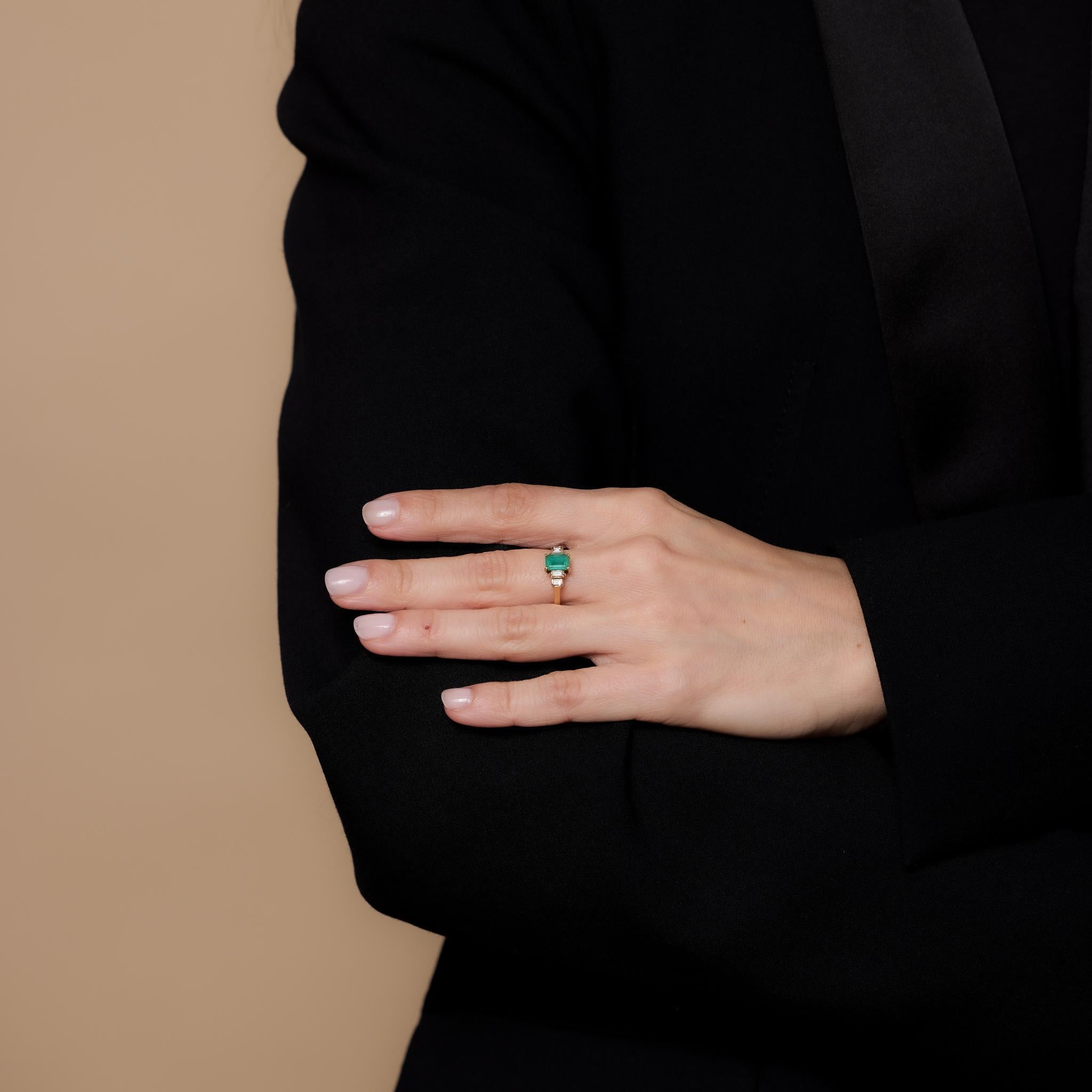 This vintage 18k yellow gold ring showcases a .80-carat emerald cut emerald, accented by four baguette cut diamonds totaling .25 carats, J color, and SI clarity. Crafted in the 1980s, it is hallmarked with a purity mark and weighs 2.77 grams.
