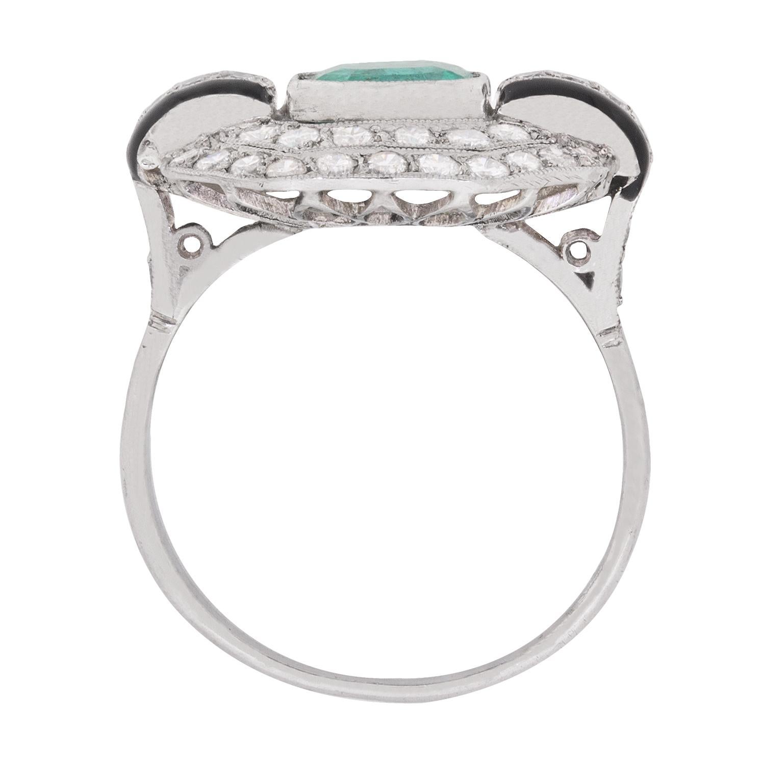 This vintage c.1950s ring, crafted in platinum and diamonds with black enamel accents, is designed around a 1.50 carat emerald.

A double octagonal halo of grain-set round brilliant cut diamonds that totals to 0.60 carats, embellishes this colourful