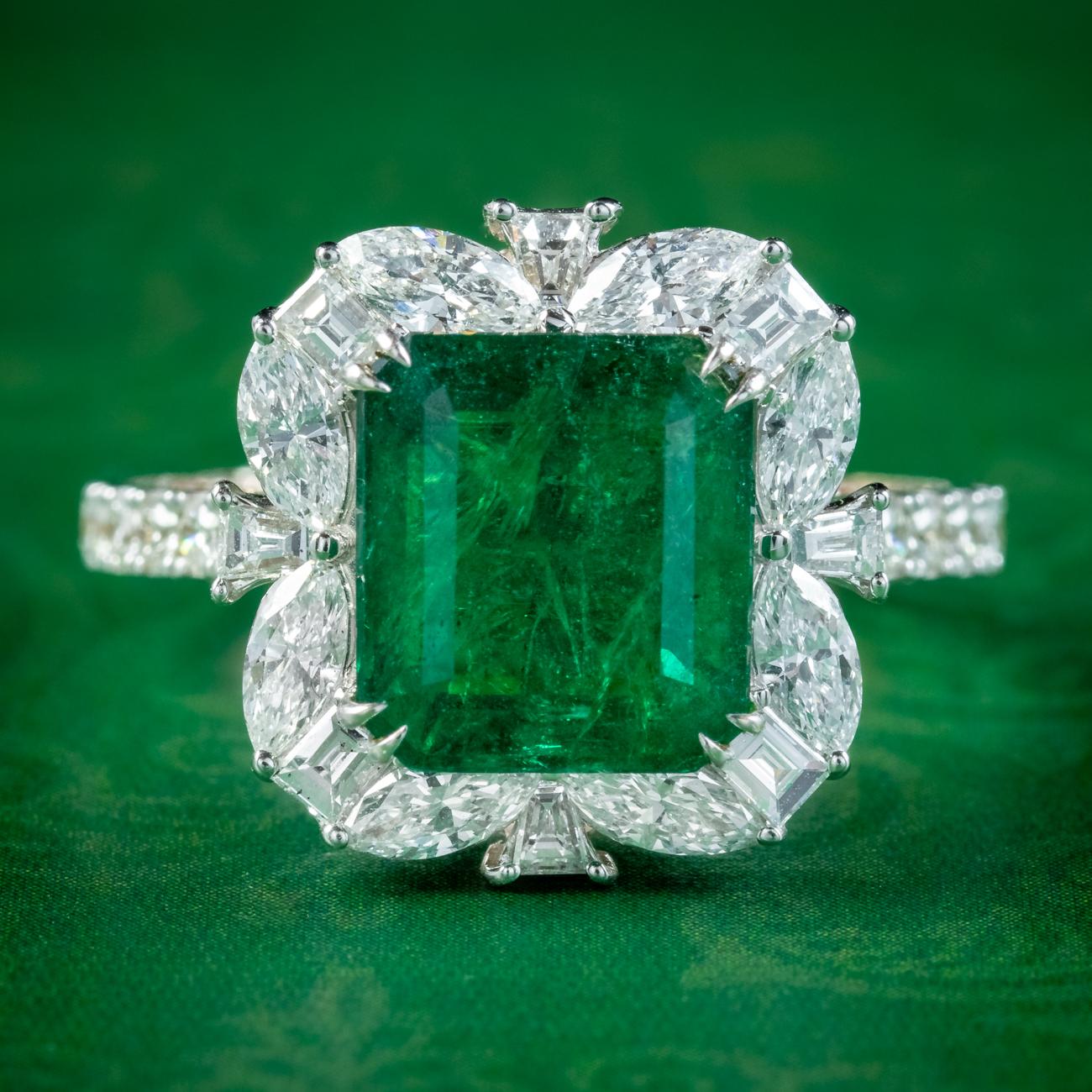 A stunning vintage cluster ring adorned with a beautiful, Brazilian step cut emerald with a particularly vivid, deep green hue. It has been tested as natural and weighed at 3.11 carats. 

The emerald is complemented by a frame of bright, clean