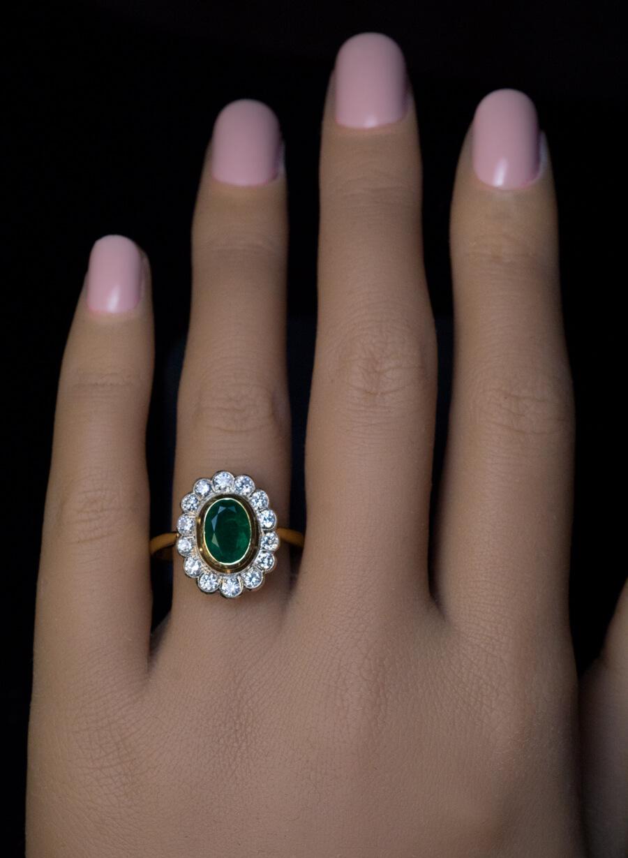 This classic cluster ring of European origin is crafted in yellow and white 14K gold. The ring is bezel set with a 1.48 ct emerald of a saturated bluish green color. The emerald is surrounded by bright white and clean brilliant cut diamonds (E-F