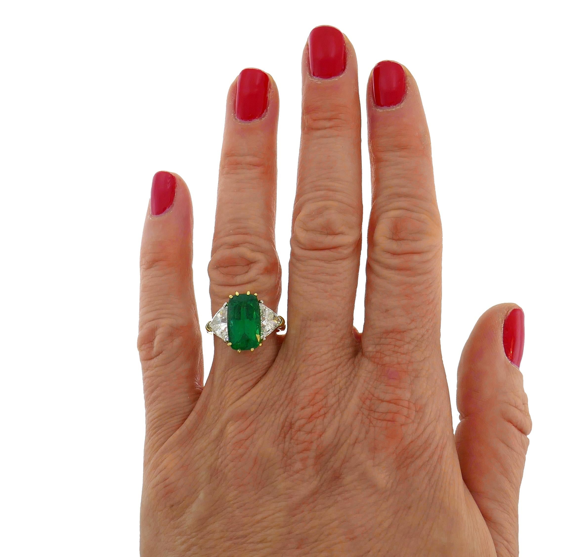 Classy and timeless three-stone ring. The ring features a beautiful cushion cut natural emerald flanked with two trillion cut diamonds. The emerald measures 13.57 x 8.02 x 6.32 mm and weights approximately 4.75-carat. It comes with a Guild