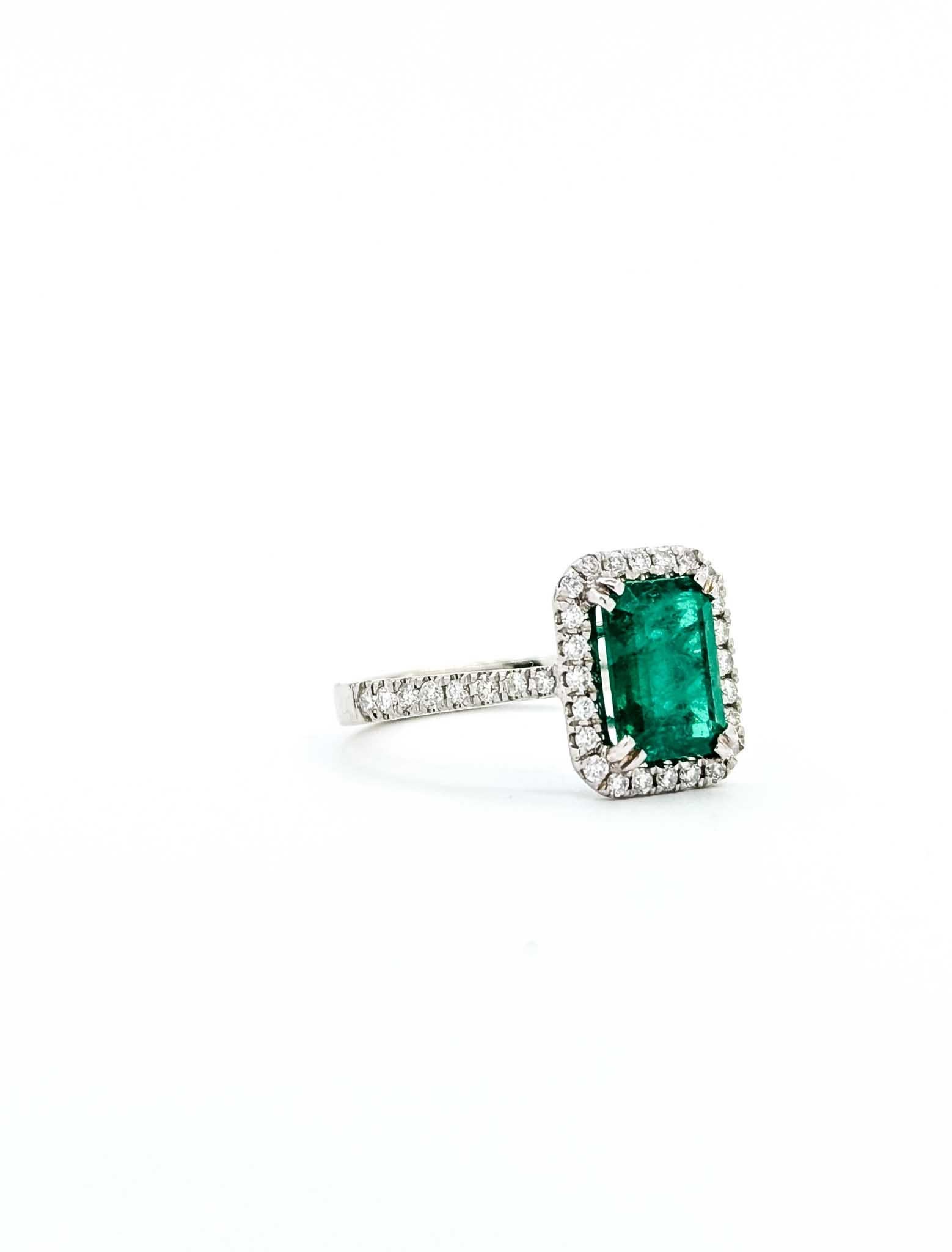 Introducing this exquisite emerald ring, crafted in luxurious 14k white gold. This captivating piece features a 1.71-carat green emerald, beautifully encircled by a halo of diamonds. The design embodies timeless elegance, with the vibrant green of