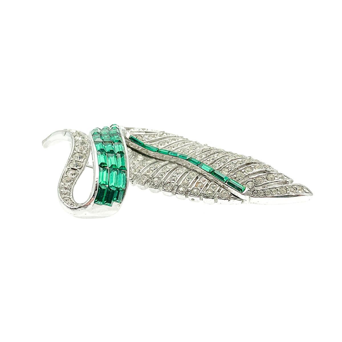 An enchanting Vintage Emerald Leaf Brooch dating to the 1950s. Featuring a deco inspired design of an undulating leaf, the many veins of which are studded with twinkling chaton crystals. Verdant emerald crystals further accentuate and trace the
