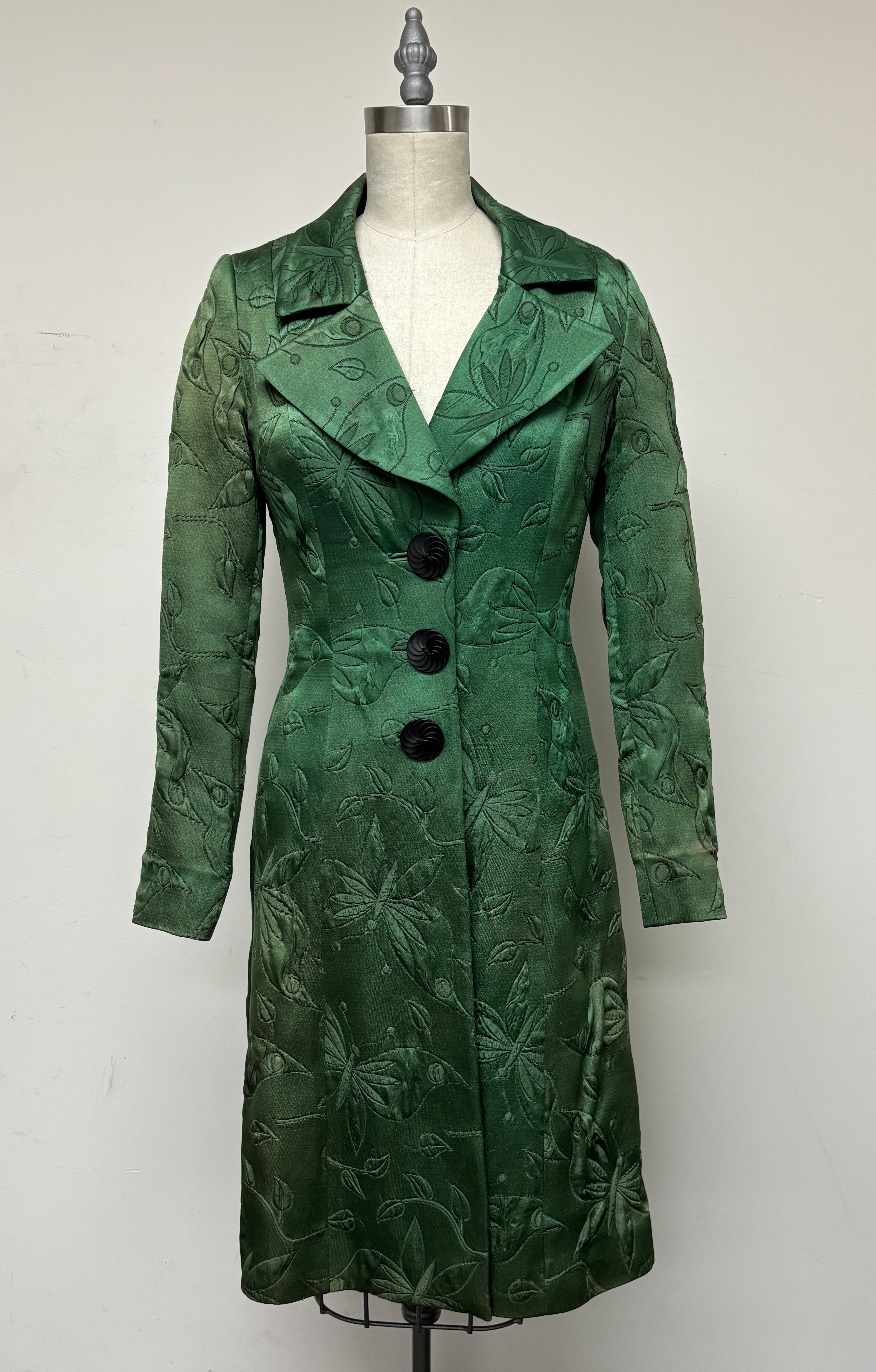 Cappotto vintage in matelasse verde smeraldo con un affascinante motivo a farfalla. Ha uno stile aderente e svasato con tre bottoni e risvolto a punta. Questo bellissimo cappotto è stato progettato per avere un colore ombreggiato con un verde