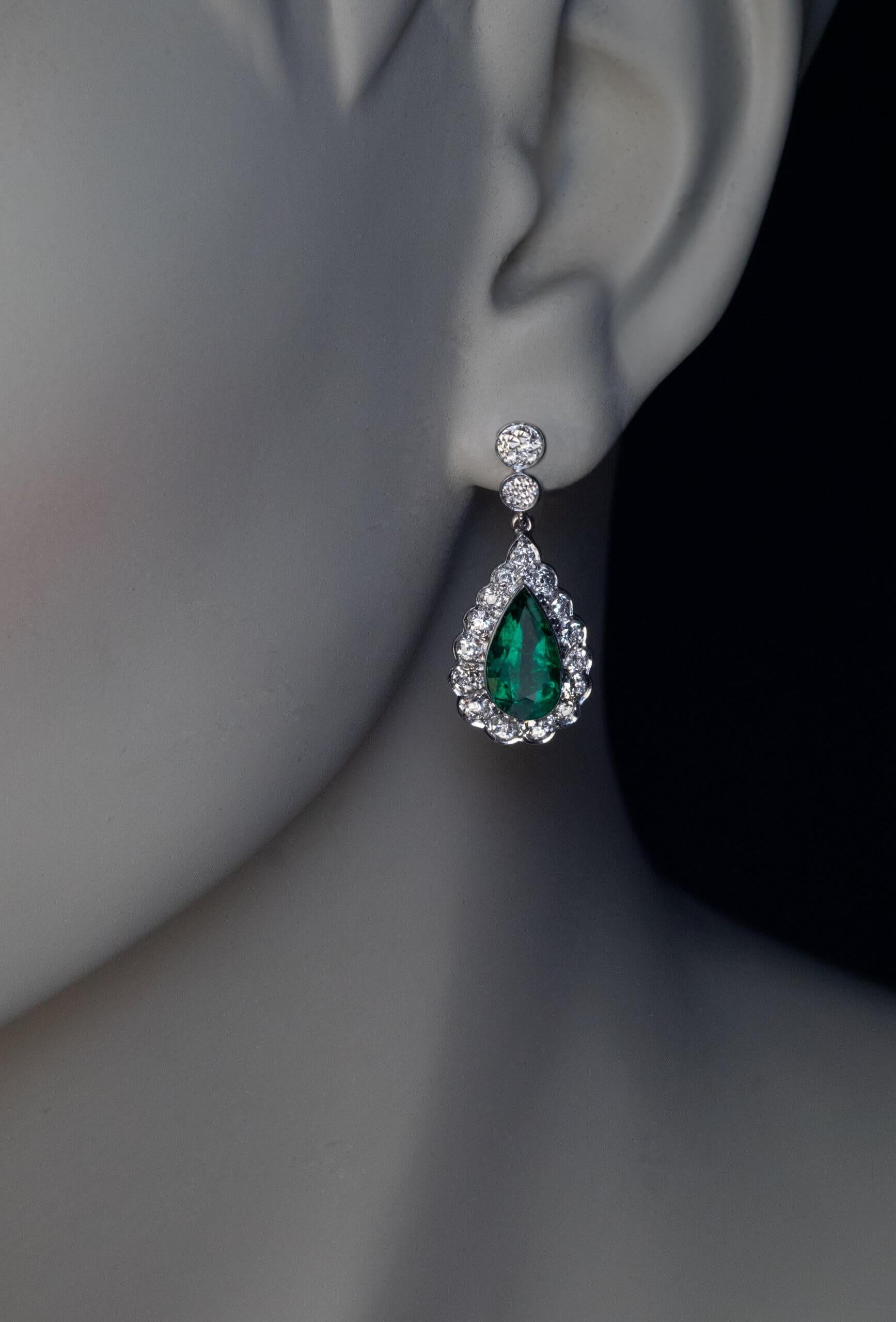 Circa 1950s  The earrings are finely crafted in white 14K gold. They feature a pair of well matched pear cut emeralds of rich bluish green color. The emeralds are set in bezels and framed by bright white and clean diamonds. Majority of the diamonds