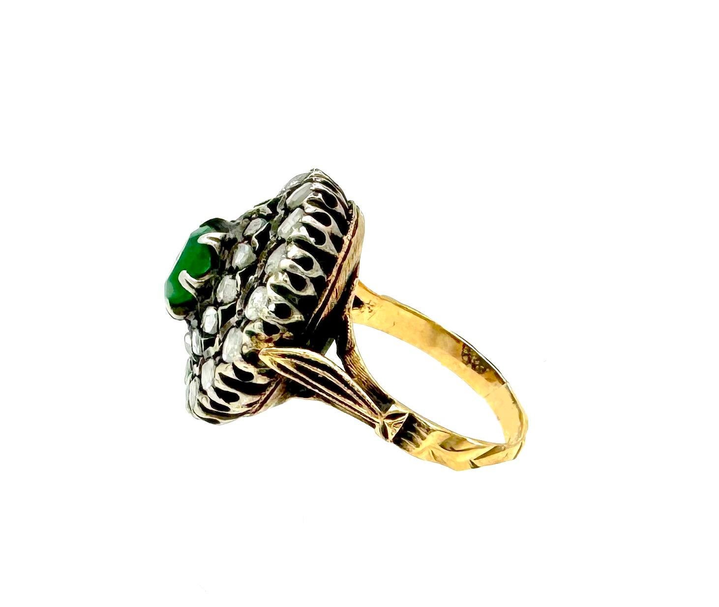 This cluster ring was created in the 3rd quarter of the 20th century in Italy out of 18K yellow and white gold. The oval emerald is set in an open claw setting. It is surrounded by twelve small rose cut diamonds within an outer frame of sixteen