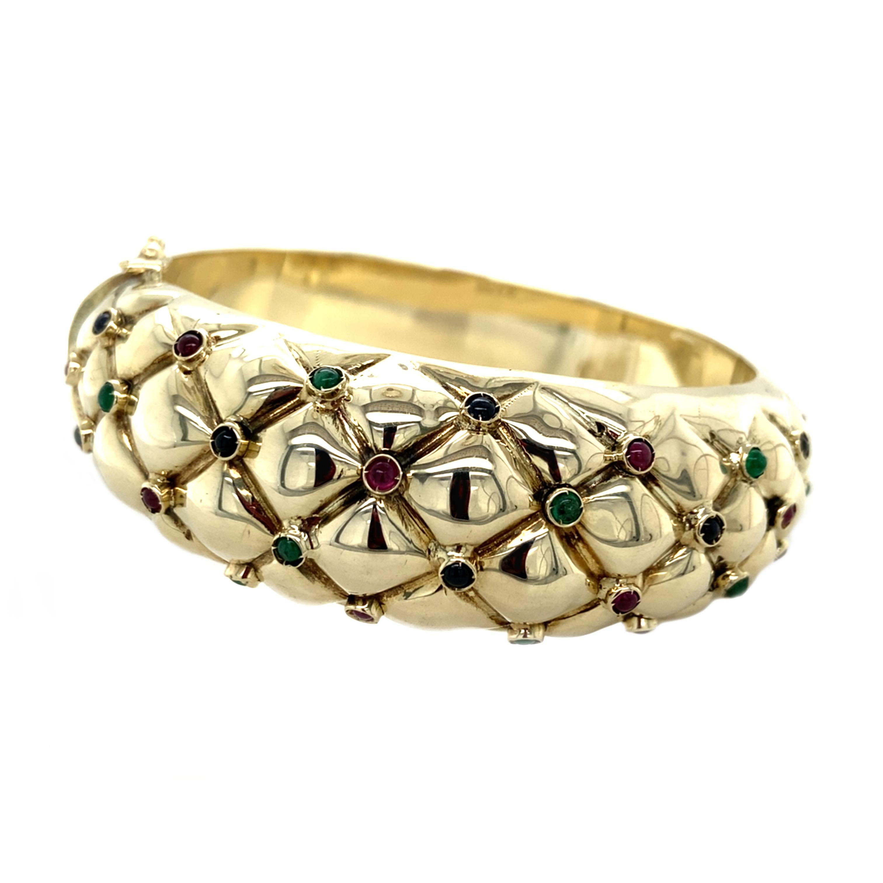Fabulously 80’s, this quilted bangle bracelet is studded with a mix of precious emeralds, rubies and sapphires in cabochon cuts. Richly colored pops of color emerge from between sculptural gold. The 80’s were all about big, bold, confident jewels
