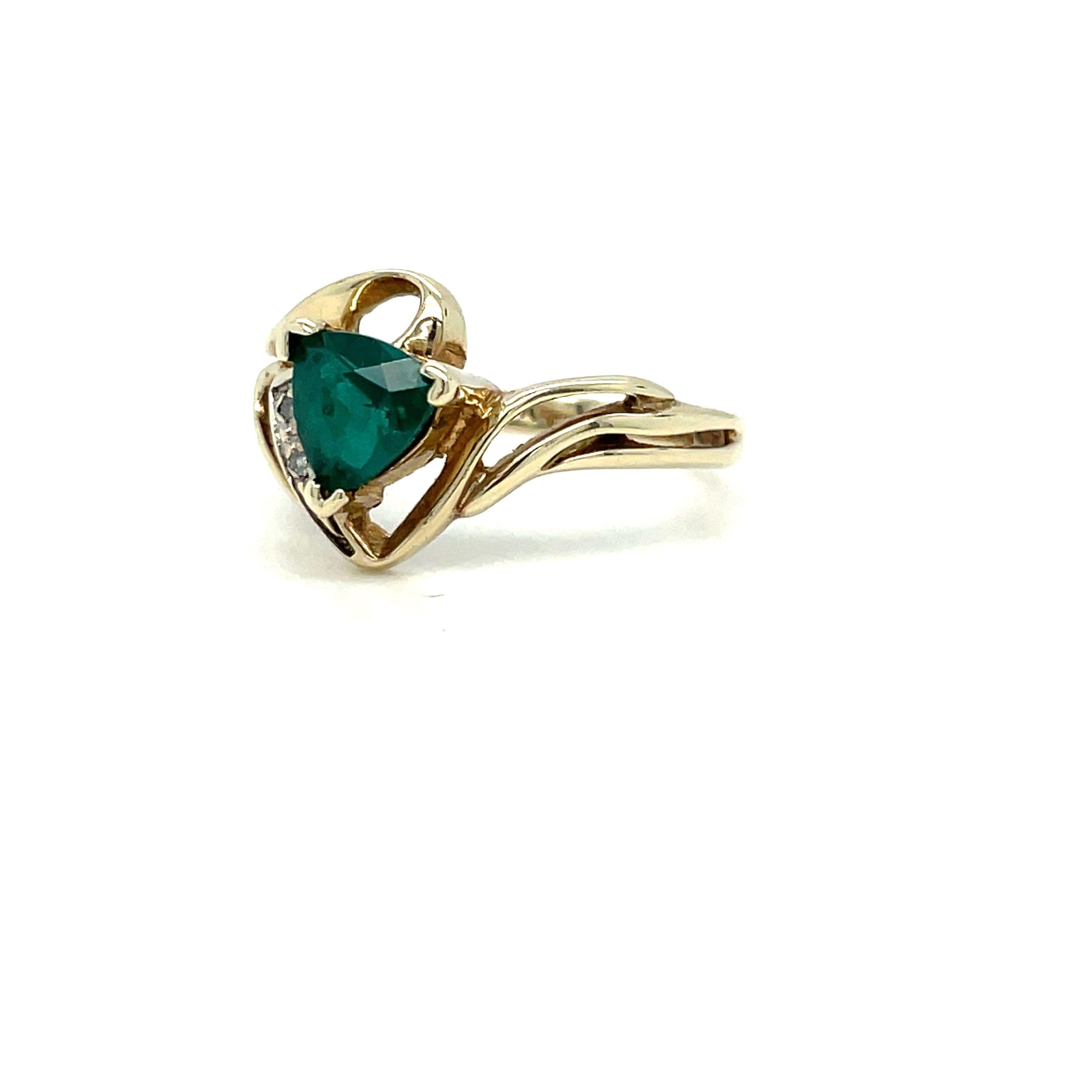 This vintage ring is absolutely stunning! It's made of 10K yellow gold and features a unique trillion-shaped emerald in the center, flanked by bead set diamonds on one side. The emerald is about 0.61 carat, and there are two round brilliant cut
