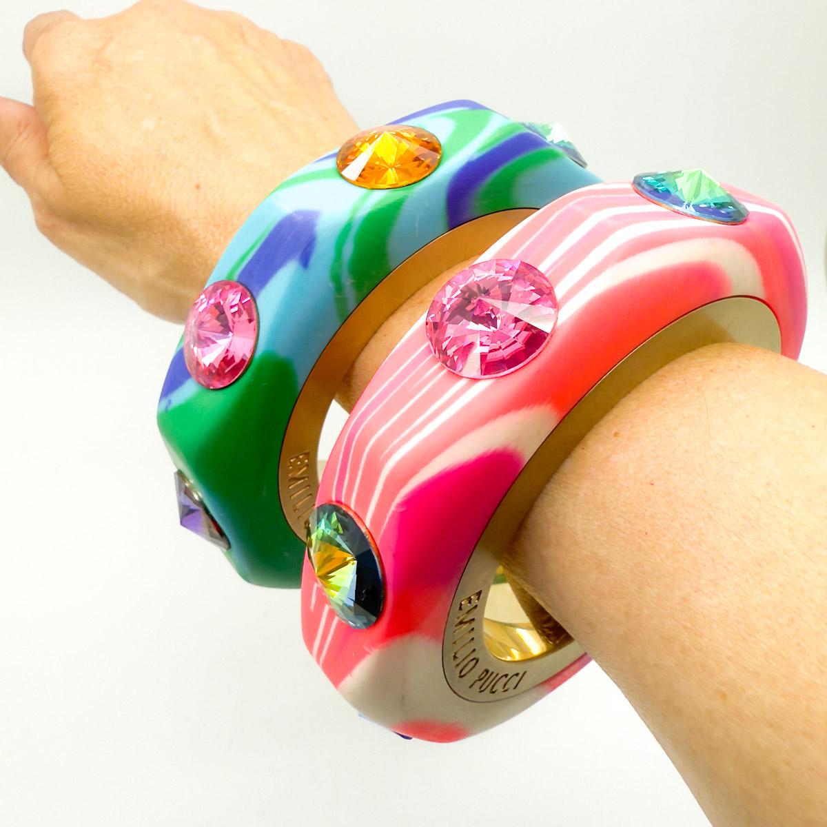 A totally amazing pair Pre-Loved Emilio Pucci Bangles. A weighty marbleised resin bangle is embellished with satin metal bands bearing the House's logo and set with large glass Rivoli crystals in wonderfully contrasting jewel brights. Stacked or