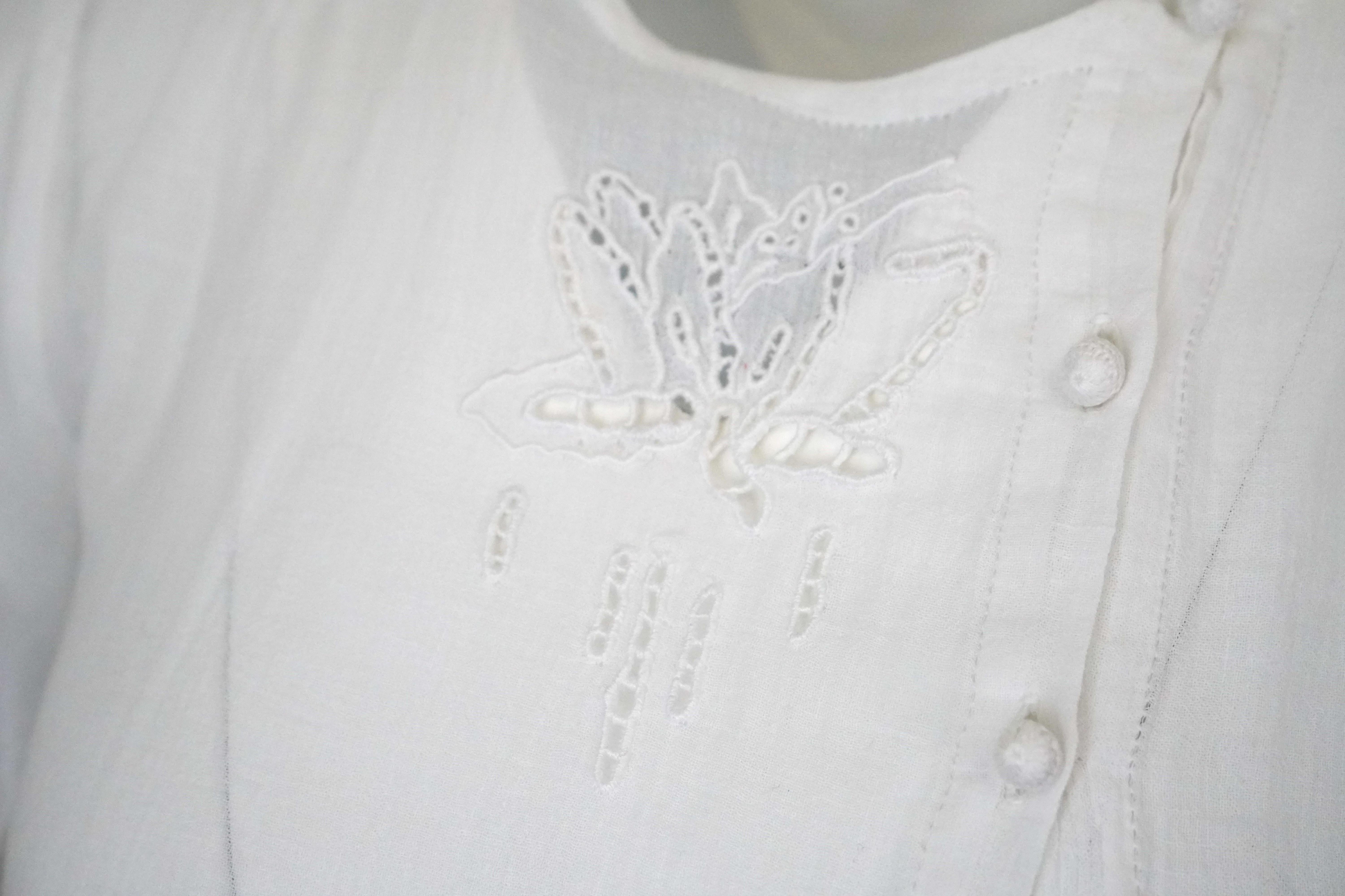 Cette rare blouse vintage en lin blanc d'Emmanuelle Whiting est en parfait état. La blouse est ornée d'une découpe à motif floral sur le devant de la poitrine et de six fermetures en forme de grenouille sur le devant gauche. Il est également doté