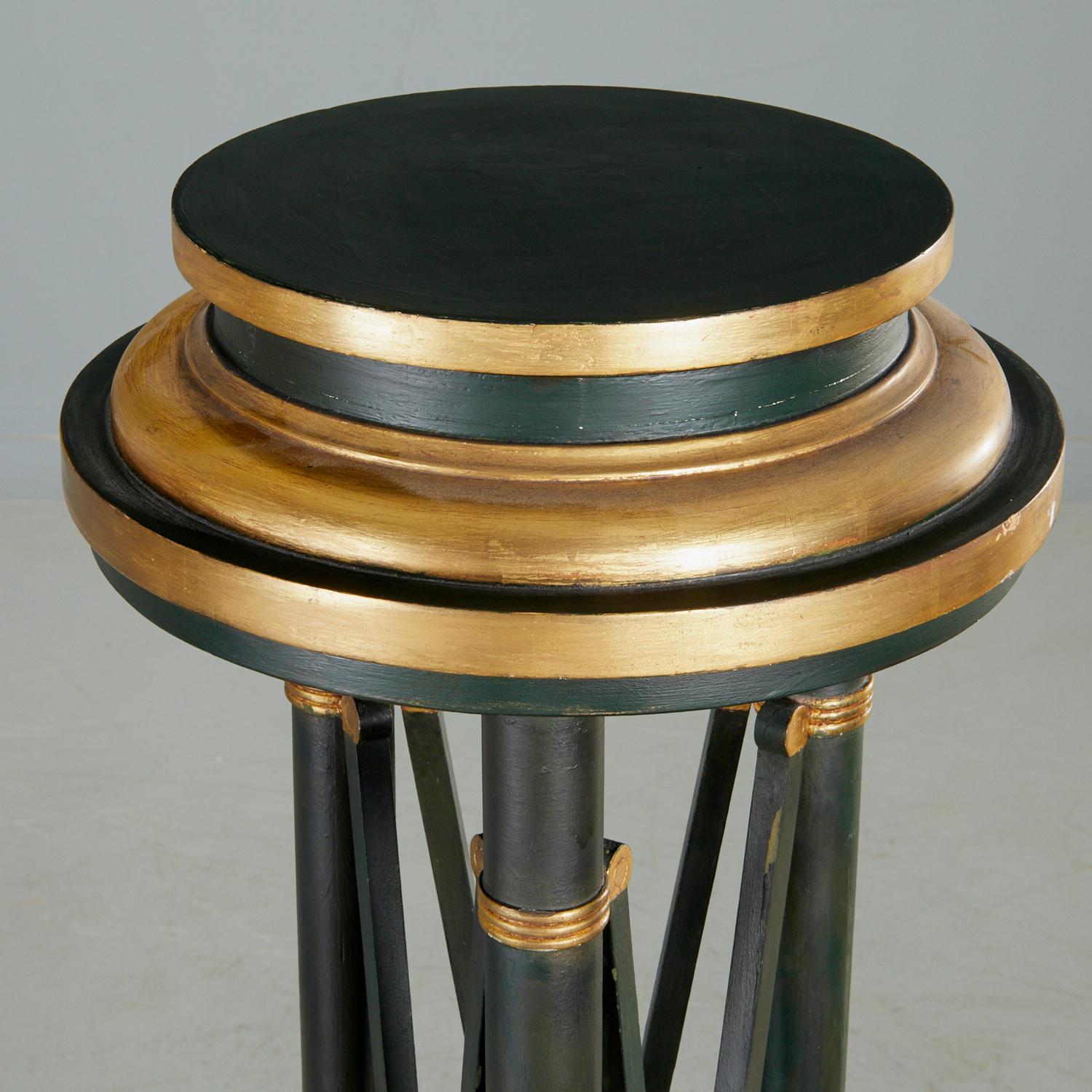 An elegant matching pair of 20th c., Continental (probably Italian) Greco-Roman style tripod stands with ebonized and parcel gilt finish, unmarked. The pedestals each have a tripod body with x-form supports on a paw feet scroll triform base. These