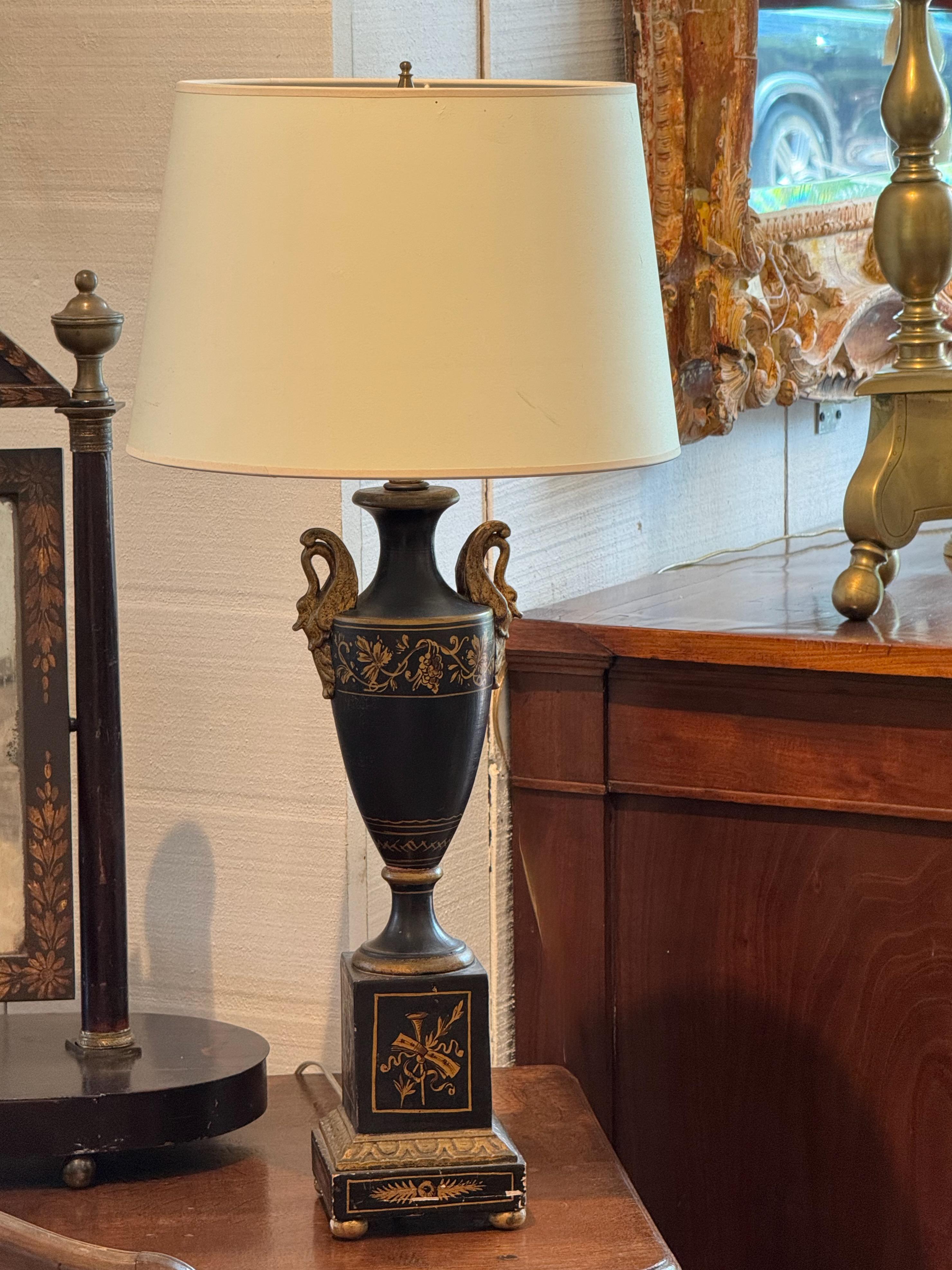 Vintage urn-form lamp in the Empire style, featuring a black-painted body with classical giltVintage urn-form lamp in the Empire style, featuring a black-painted body with classical gilt detailing and decorative swan-form handles. The square base is