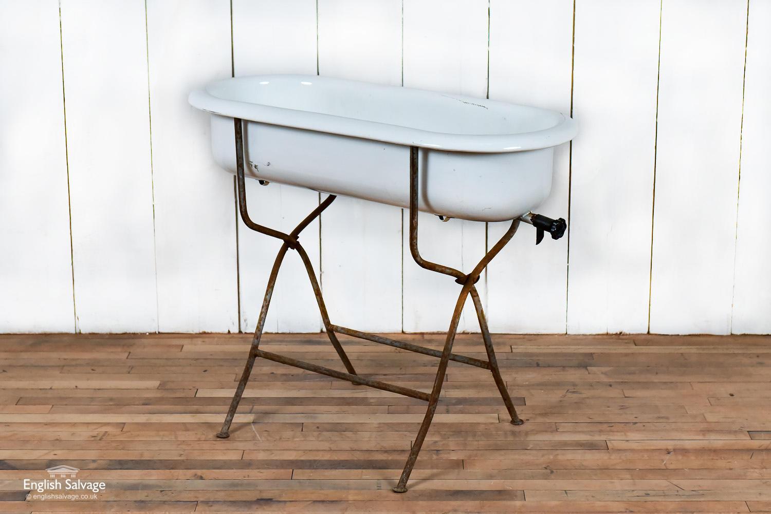 Vintage child's bath on a metal stand. The stand has an appealing patina with surface rust and grey paint. The bath itself has a few minor scratches but appears to be in sound condition. Overall dimensions are given below and the bath tub without