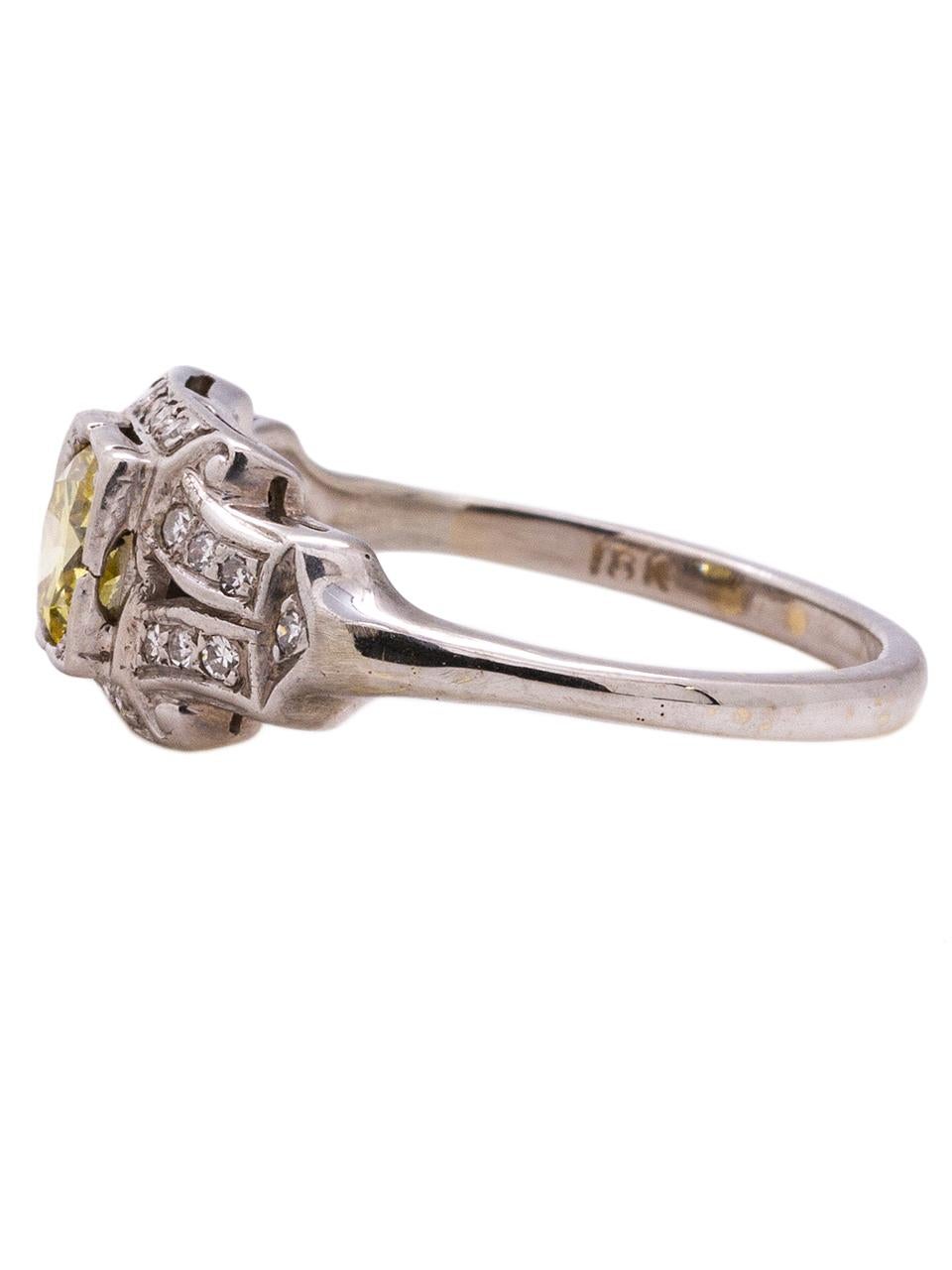 Classic Art Deco vintage 18k white gold engagement featuring a stunning 0.59ct fancy intense yellow, VS2 transitional cut round diamond. Twenty two bead set single cut side diamonds adorn the architecturally designed setting. The relatively low