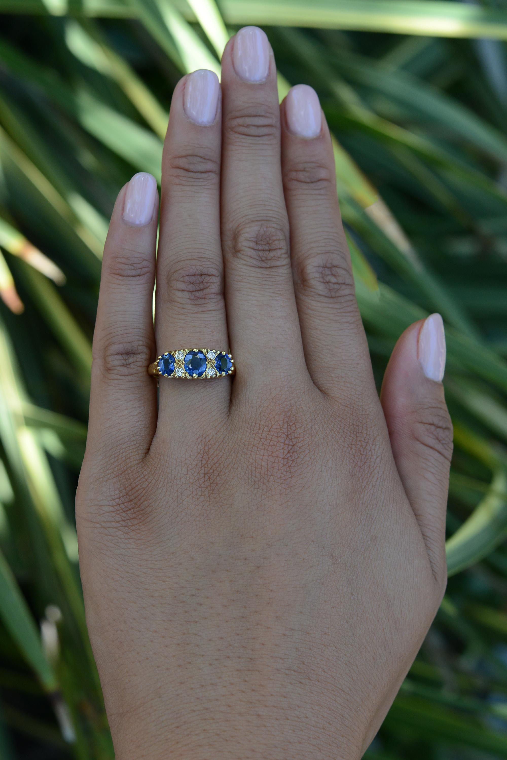 Adorn your finger with this fabulous vintage Victorian English 3 stone sapphire engagement ring. Crafted from 18 karat yellow gold, the trilogy of vivid royal blue sapphires are nested between 4 sparkling diamonds amongst a scroll work gallery.