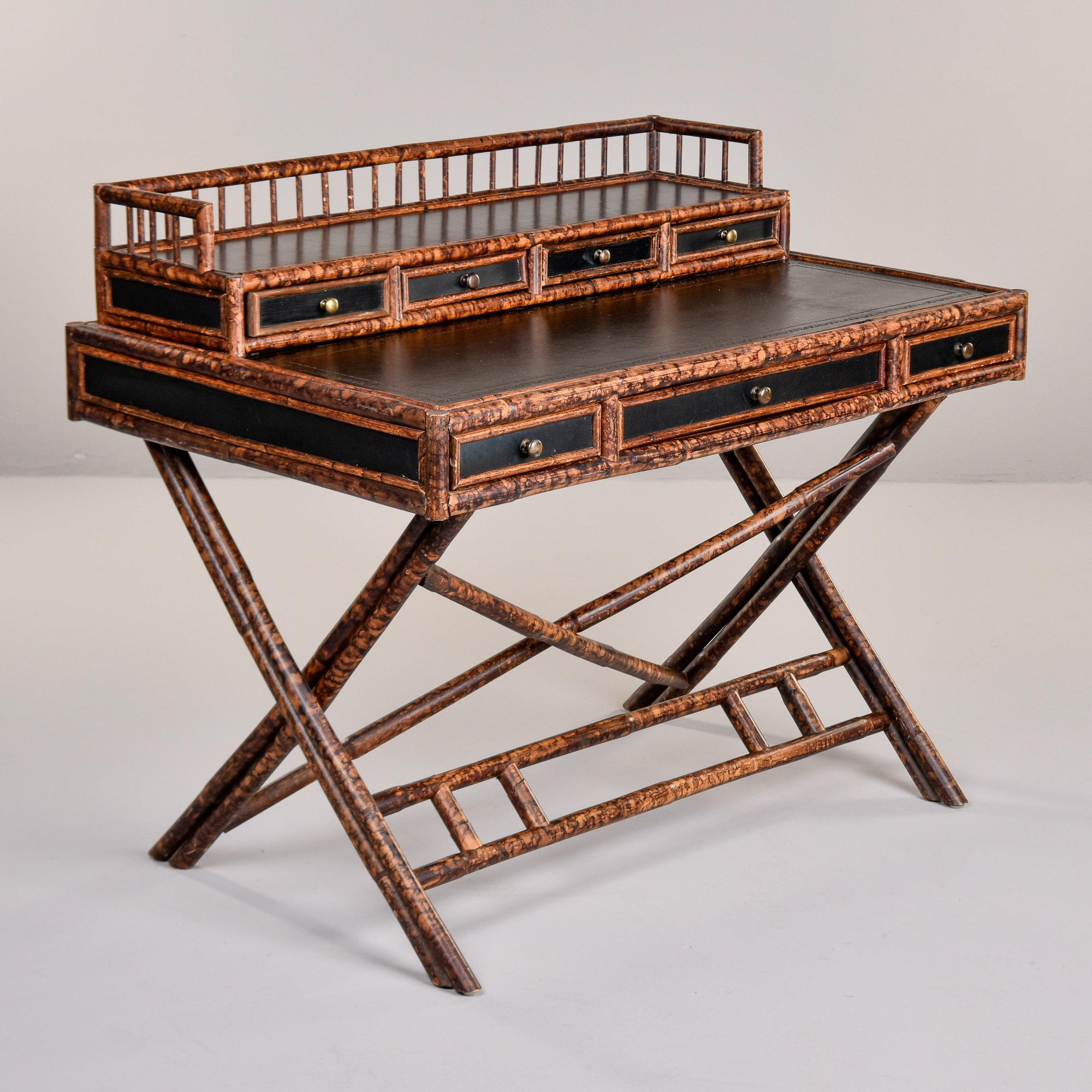 Found in England, this vintage Aesthetic style bamboo desk dates from the 1960s. X-Form spotted bamboo base supports a two tier desk top. Lower tier has a black leather writing surface with black sides and drawer fronts trimmed in bamboo. Three