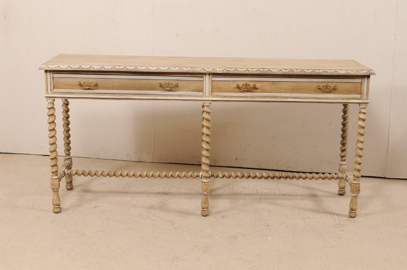 A vintage English ashwood console table with drawers. This English table features an elongated rectangular top with nicely detailed carving along it's edge, a slender case body which houses two drawers. The table is presented upon three pair of long