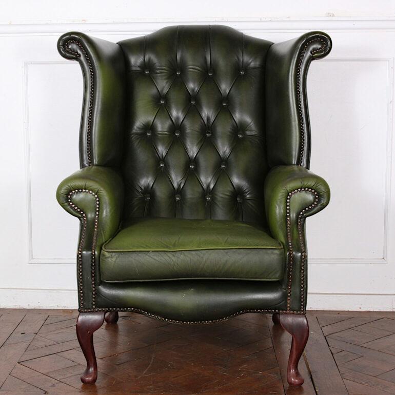 A vintage classic English-made button tufted leather wing back armchair with rolled arms and brass stud details.