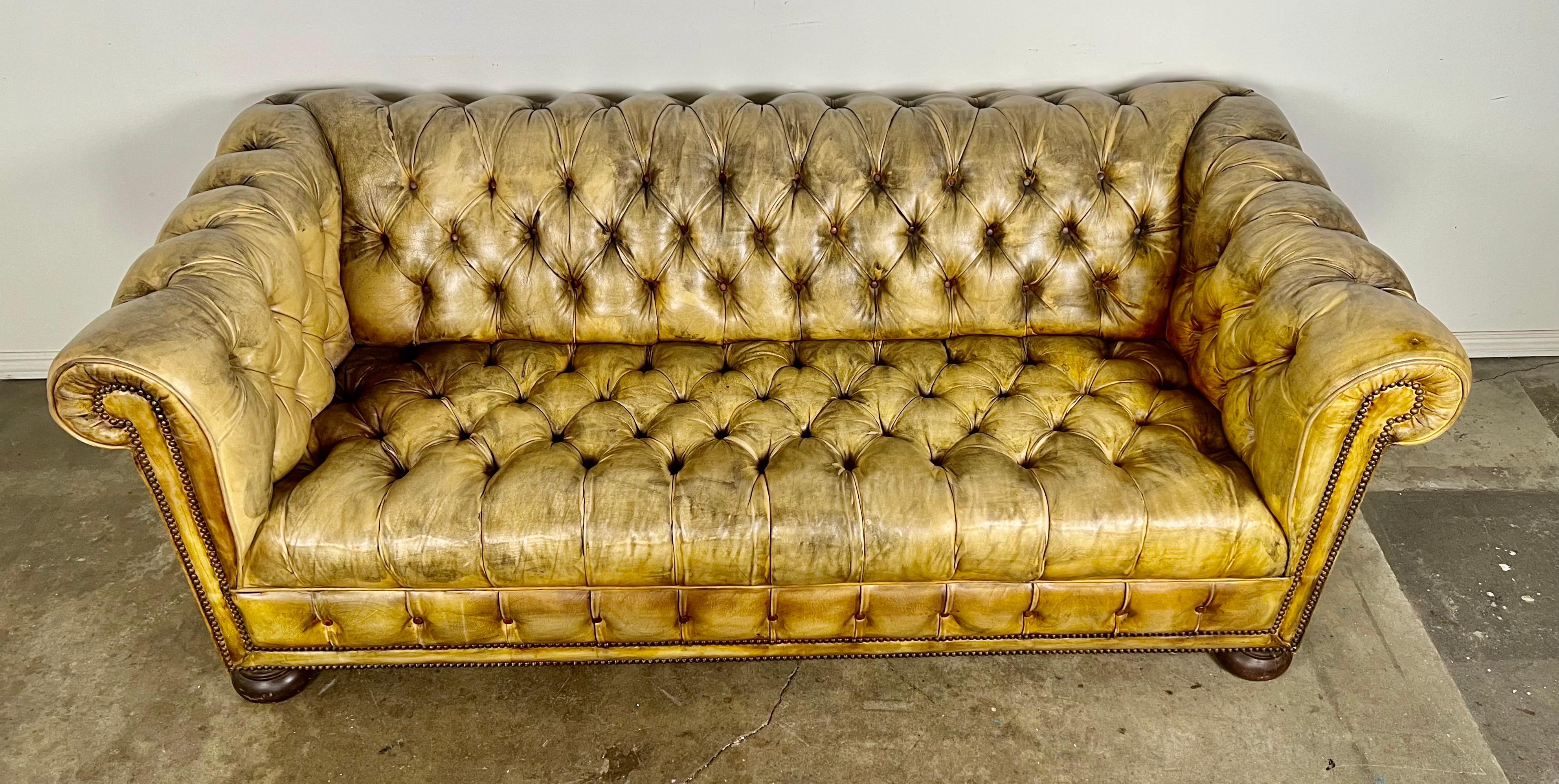 Vintage English Chesterfield style leather tufted sofa with bun feet.  The Chesterfield sofa has nailhead trim detail throughout.  This sofa has developed a beautiful patina from years of use.