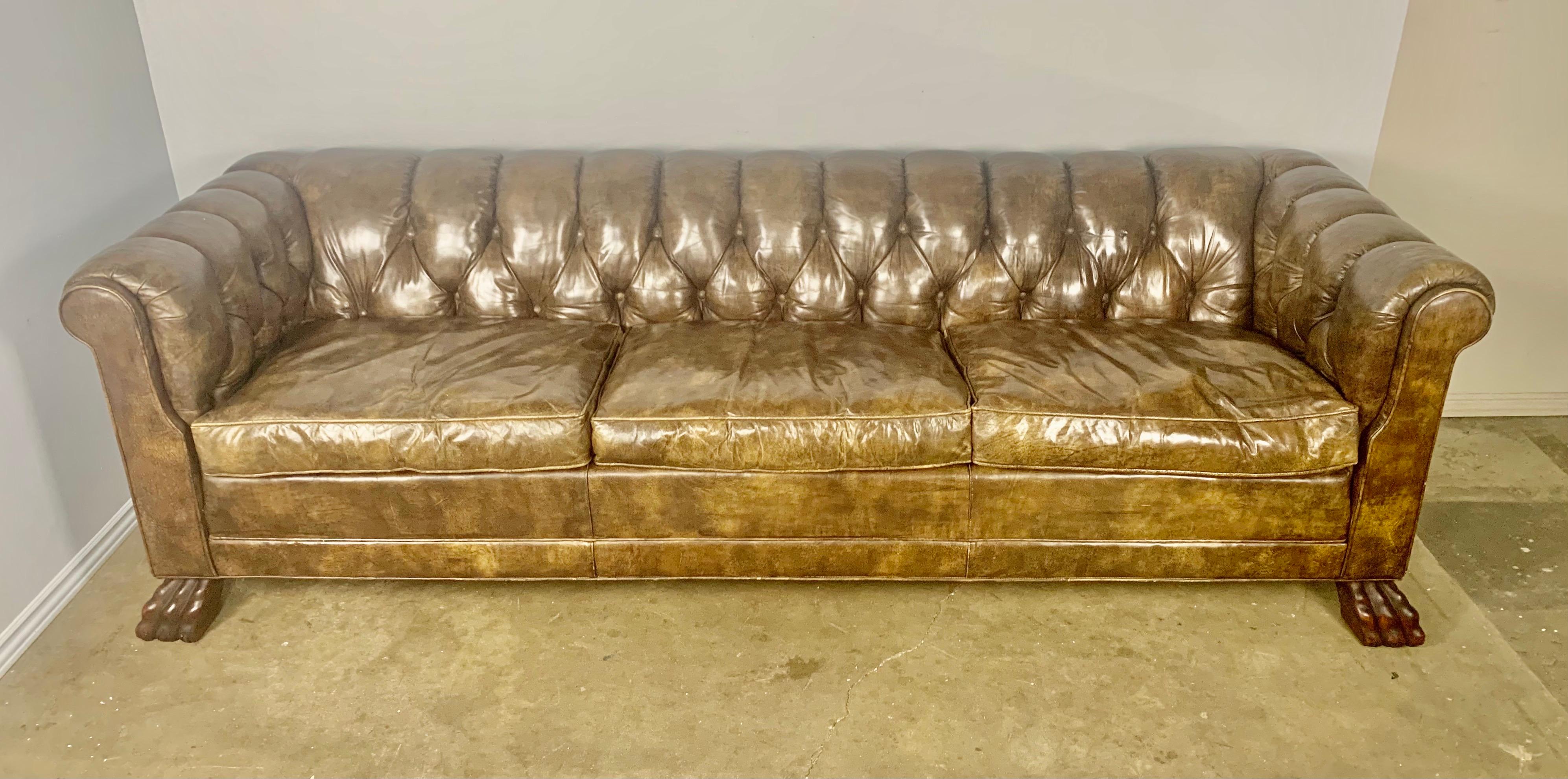 Vintage English tufted Chesterfield style sofa with loose seat cushions. The back and arms are tufted and the leather is beautifully worn. The sofa stands on four hand carved lion paw feet.
