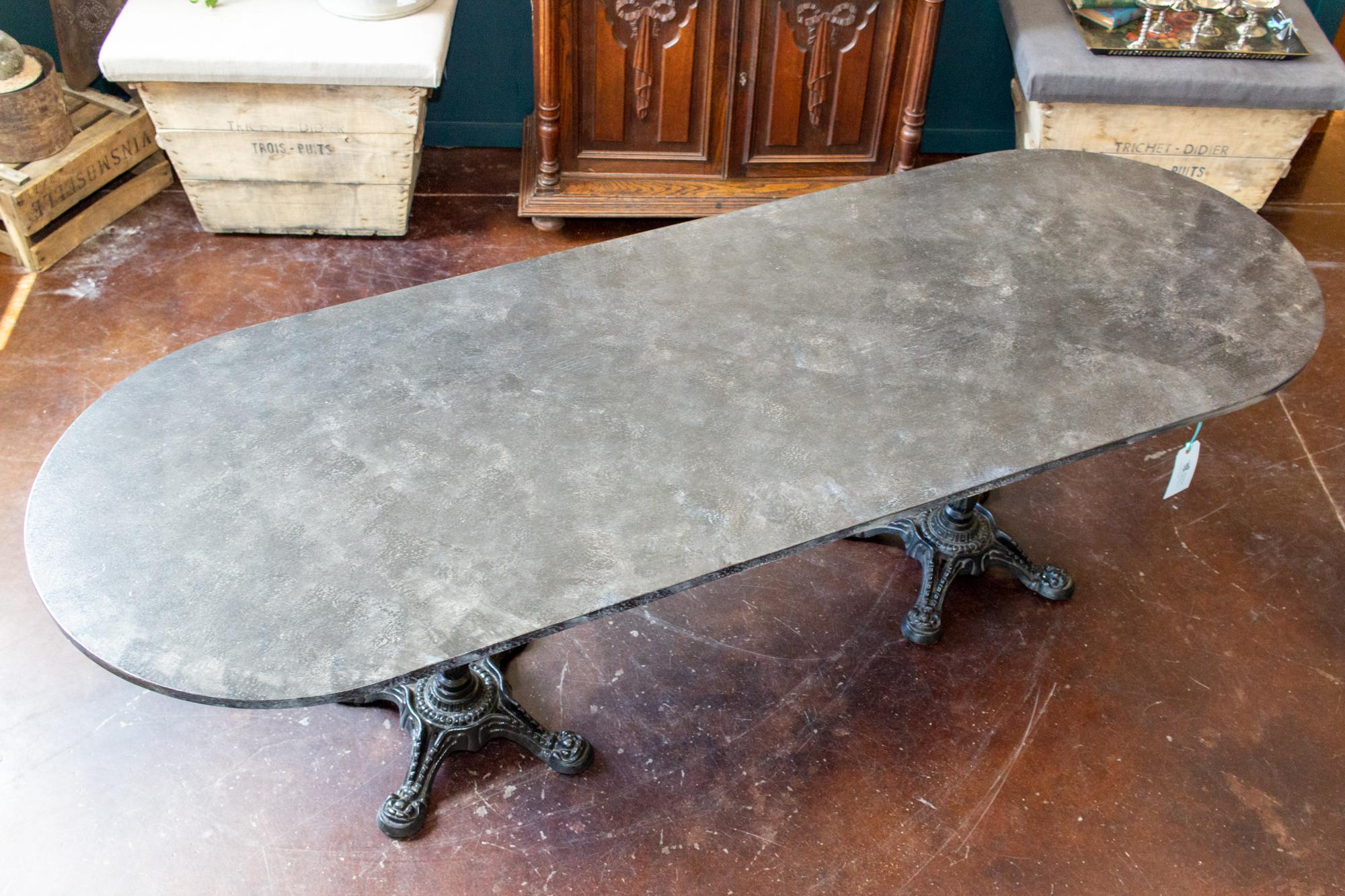 This stunningly painted wood and iron extra long bistro-style table was sourced in England. The top is ovular, with a faux marble stone finish and the top rests on top of two matching French cast iron bases. There are some small losses to the edge