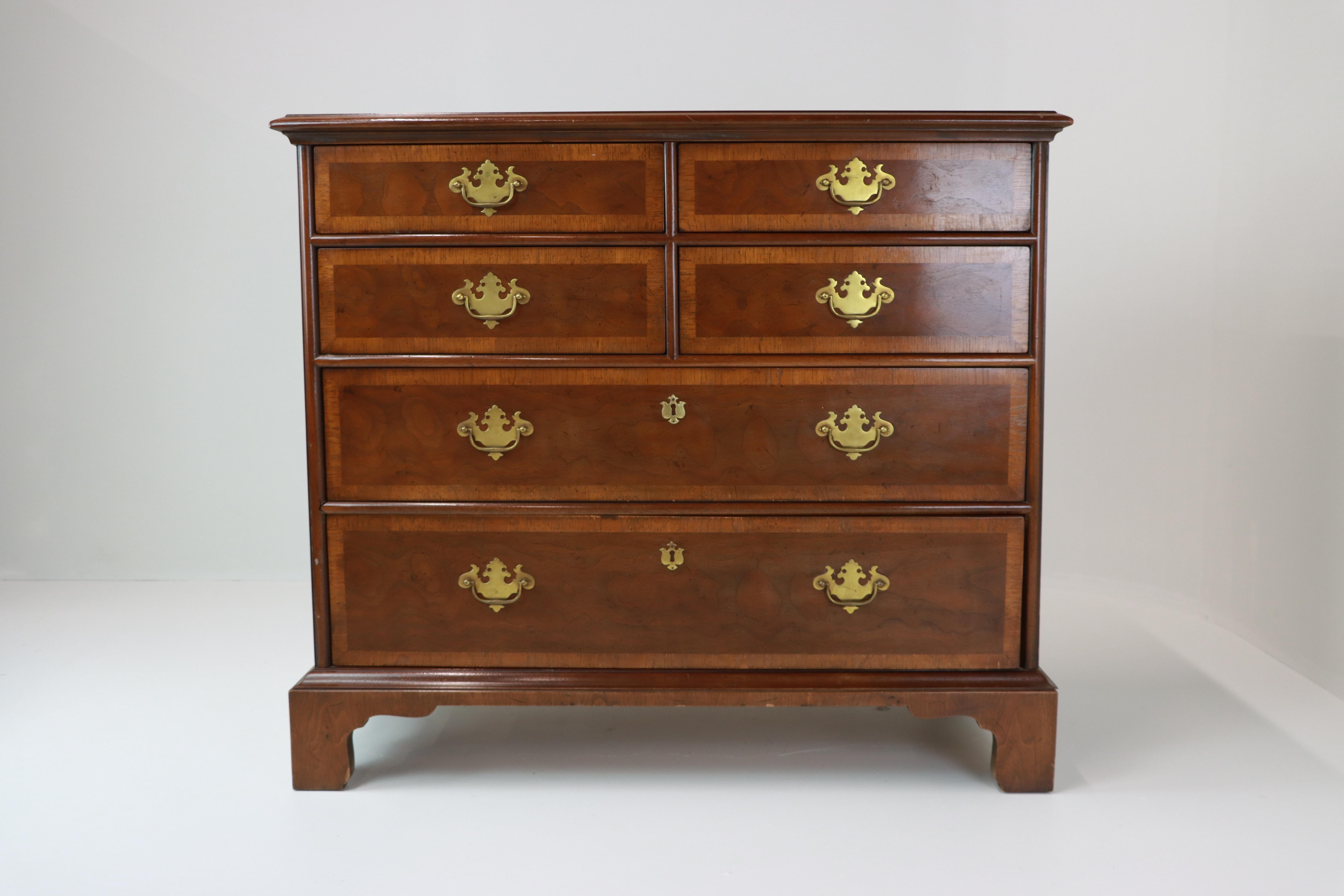 A finely made Georgian Revival chest of drawers, echoing the elegance of late 18th century George III furniture. The top sits above two short drawers over three graduated long drawers, each with brass batwing handles and escutcheons in period style.