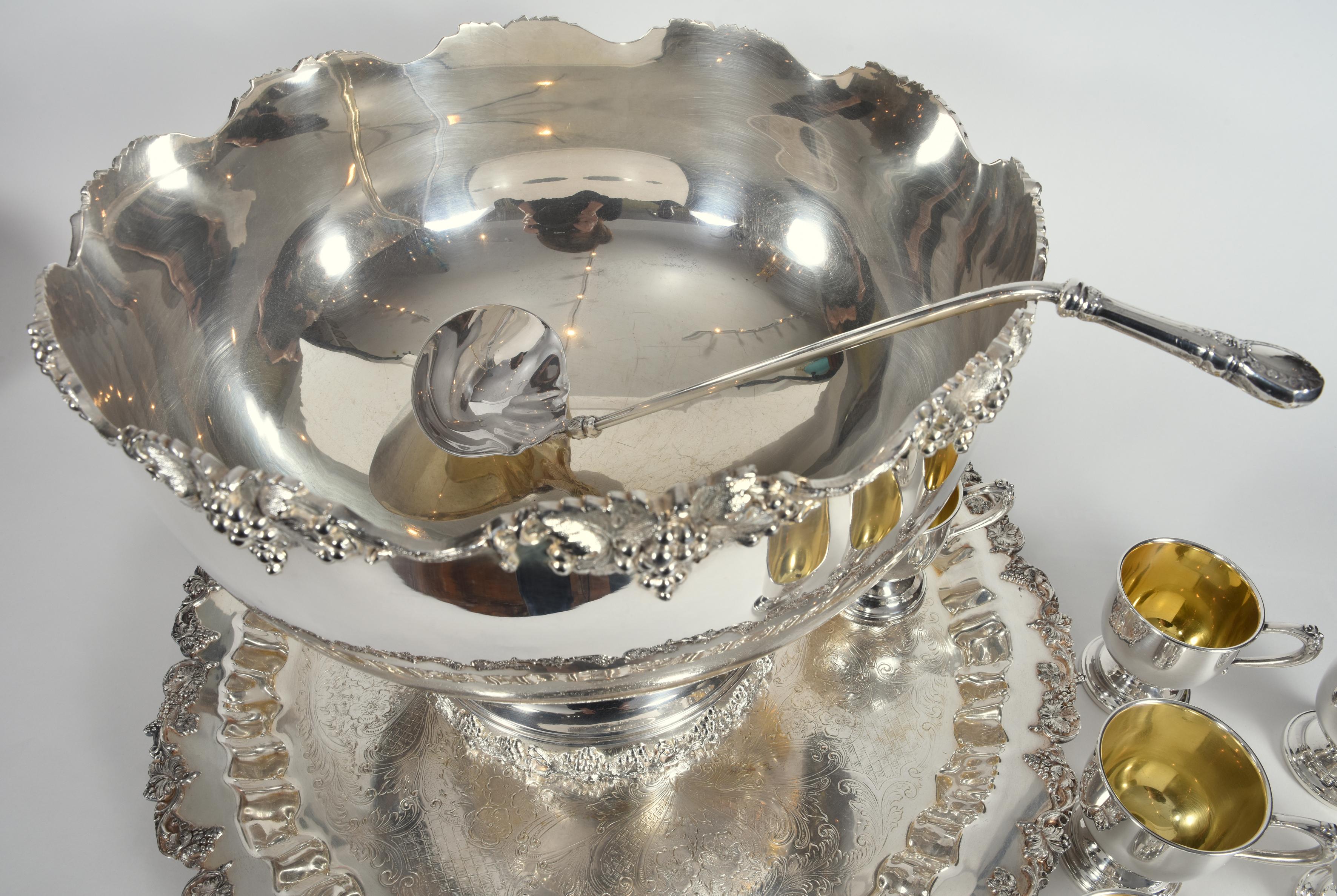Vintage English Georgian style silver plated or copper fifteen piece punch bowl set, complete with twelve decorative cups with gold wash interior and ladle. The bowl with round holding serving tray are highly decorated with incorporating stylized