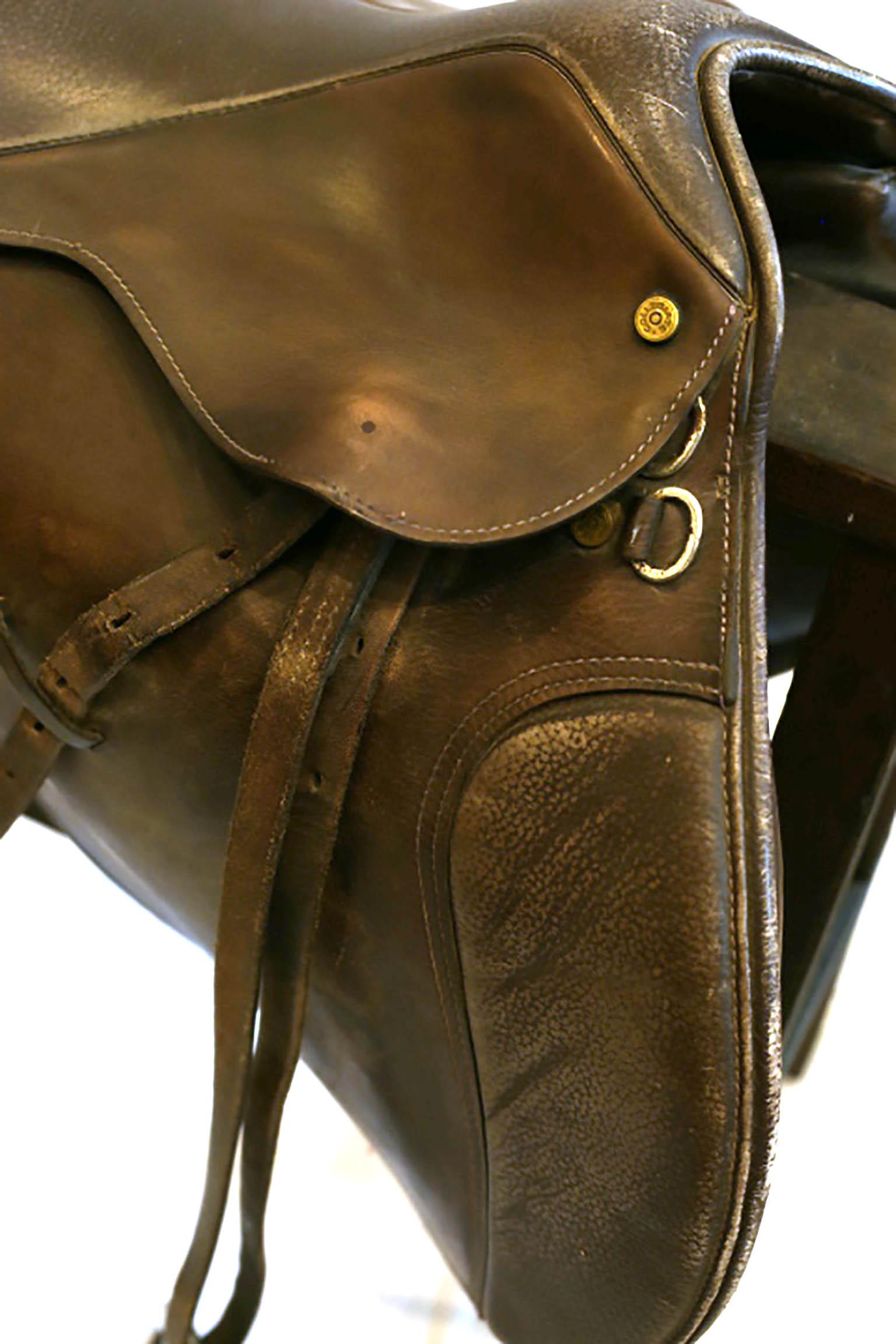 Beautiful English riding saddle with metal stirrups by Collegiate and small wooden sawhorse.