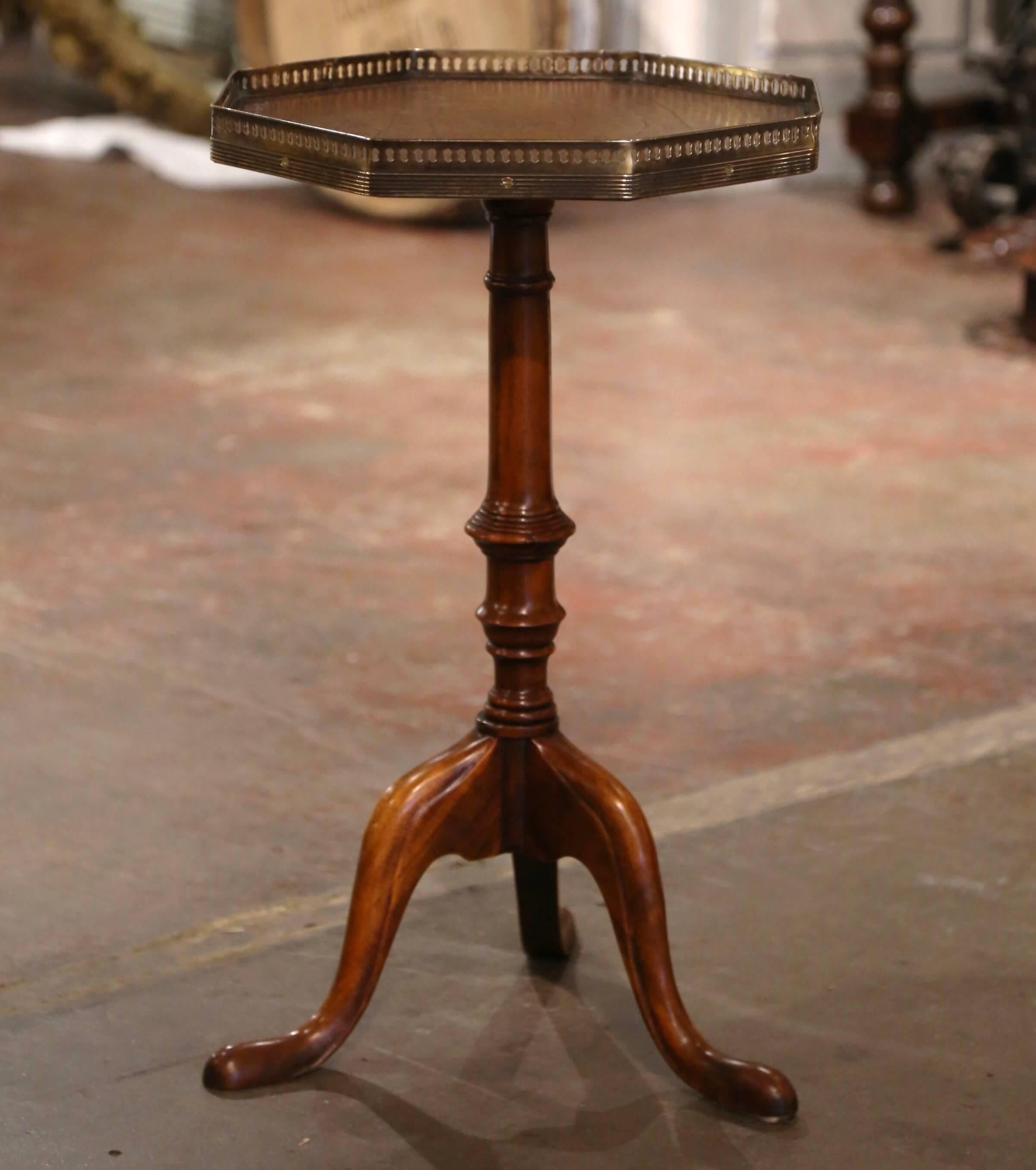 Decorate a den or living room with this elegant side table. Crafted in England circa 1990, the table stands on a carved turned pedestal base ending with three scrolled legs; the octagonal surface is dressed with a brown leather top decorated with