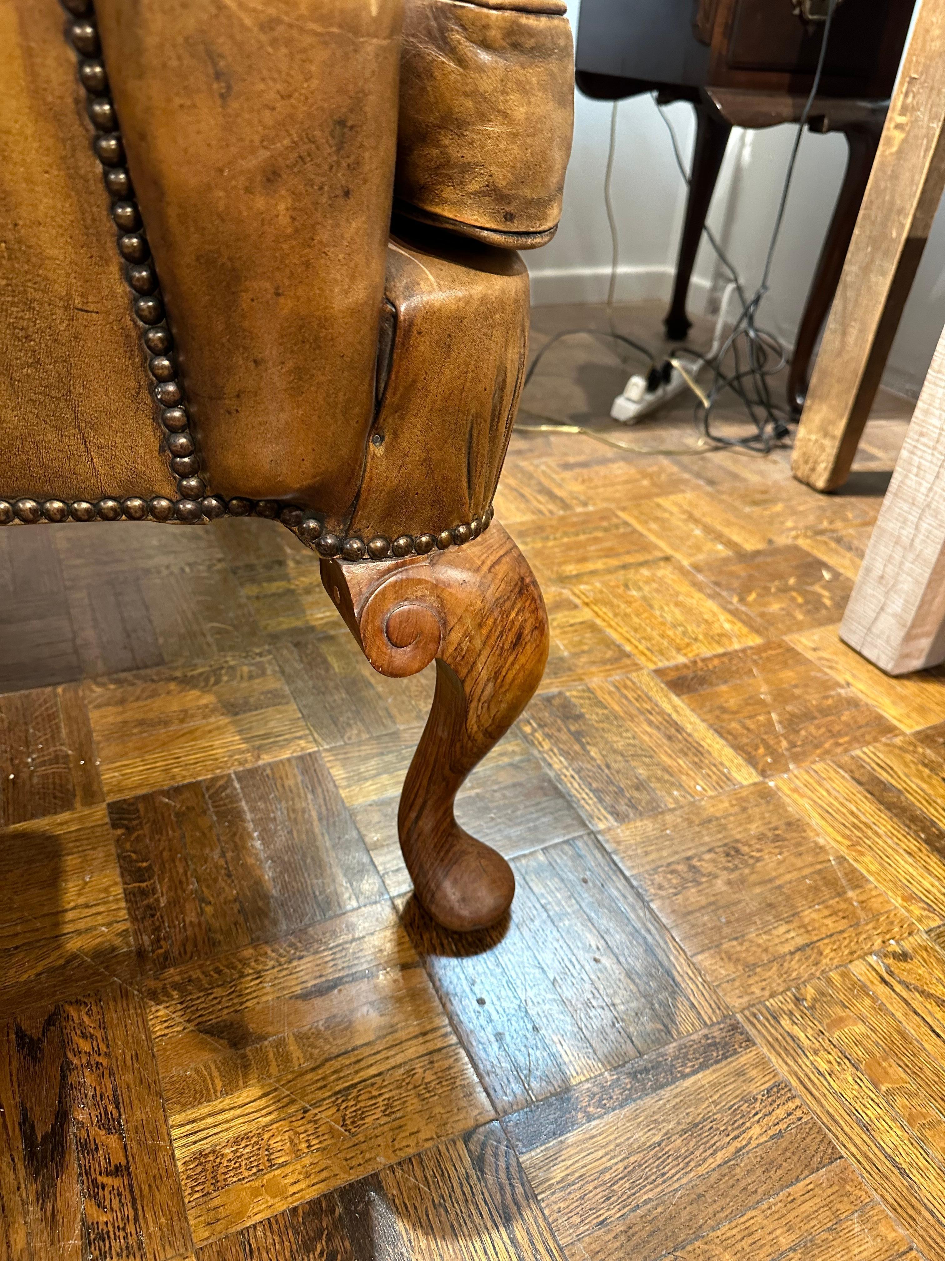 Custom hand made in London England in 1960s.  Wonderfully patinated leather wingback chair with loose cushion.  Very comfortable seat and back, beautifully tufted with ample arms.  
Hard oak wood hand carved legs in Queen Ann style.
This is the very