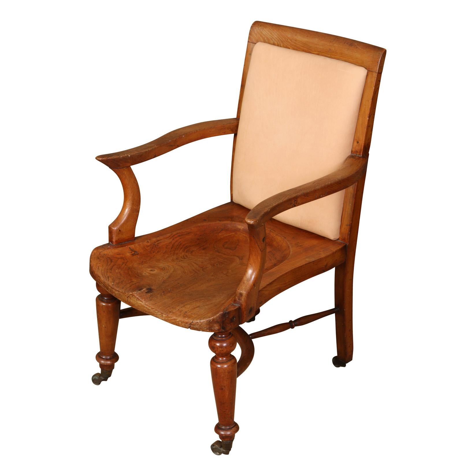 An English vintage armchair with a straight back, curved arms and turned legs ending in casters. The seat back has an inset upholstered cream leather pad and the seat is comfortably shaped without a cushion. The arms are each curved and end with