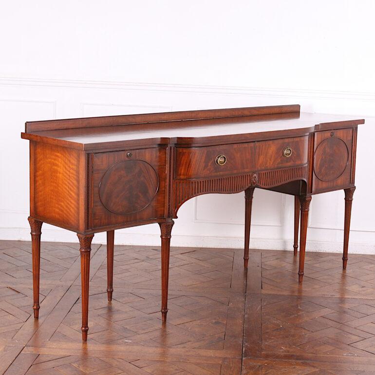 Lovely-quality vintage English-made Sheraton style sideboard or buffet, fitted with a pair of cabinets flanking a generous central drawer, all with oval flame mahogany veneered panels. Elegant fluted details to the skirt and raised on turned