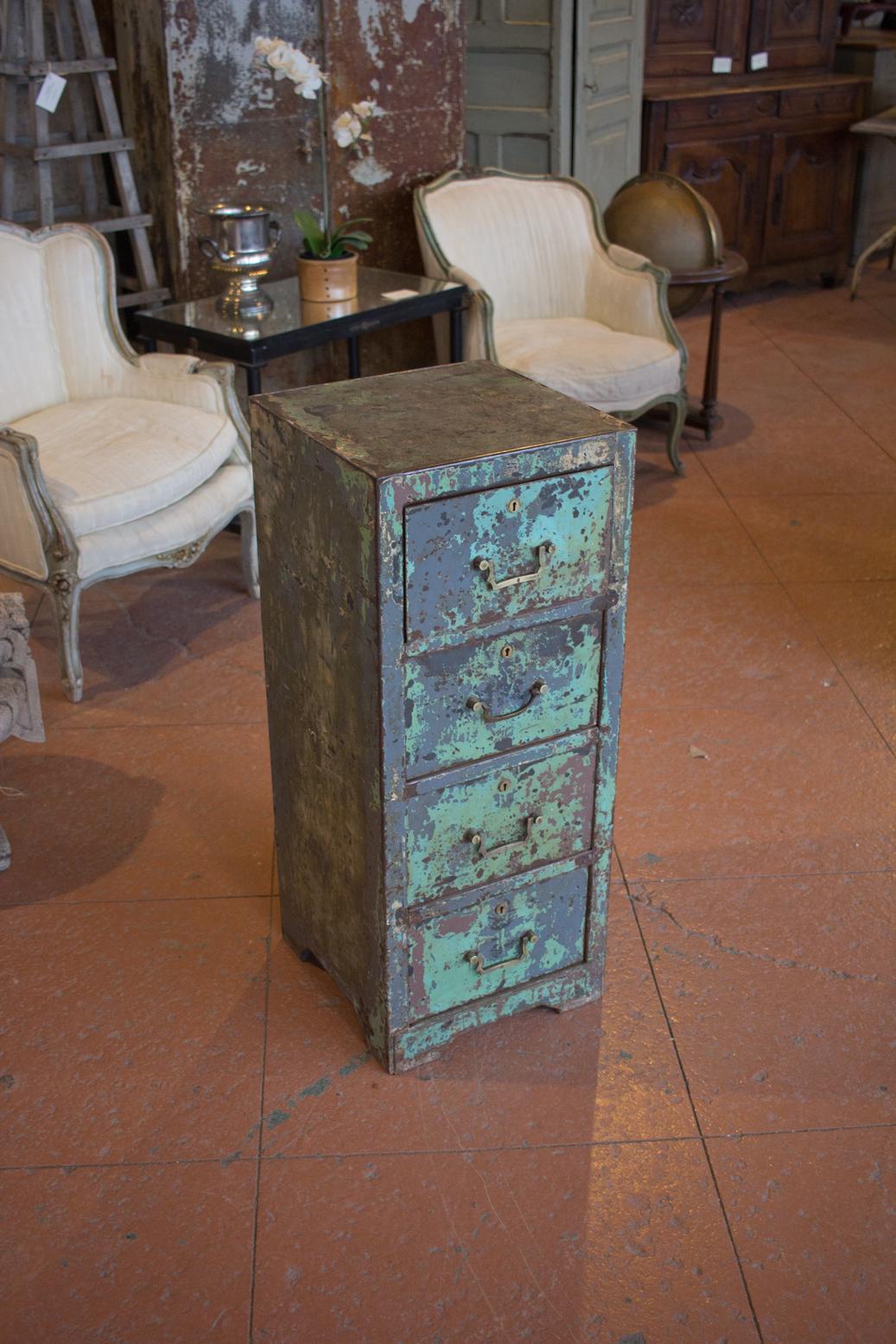 Vintage English metal filing cabinet. There are layers of residue old paint that has been sealed. It has 4 deep drawers, each one with brass handle and key hole.