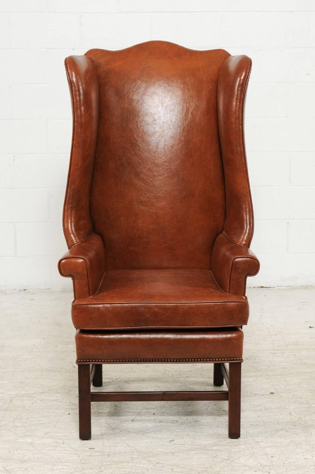 An English vintage brown leather wingback chair with straight legs and side stretchers from the mid-20th century. This English wingback chair is upholstered in a warm brown leather, accented with a discreet brass nailhead trim on the outside. The