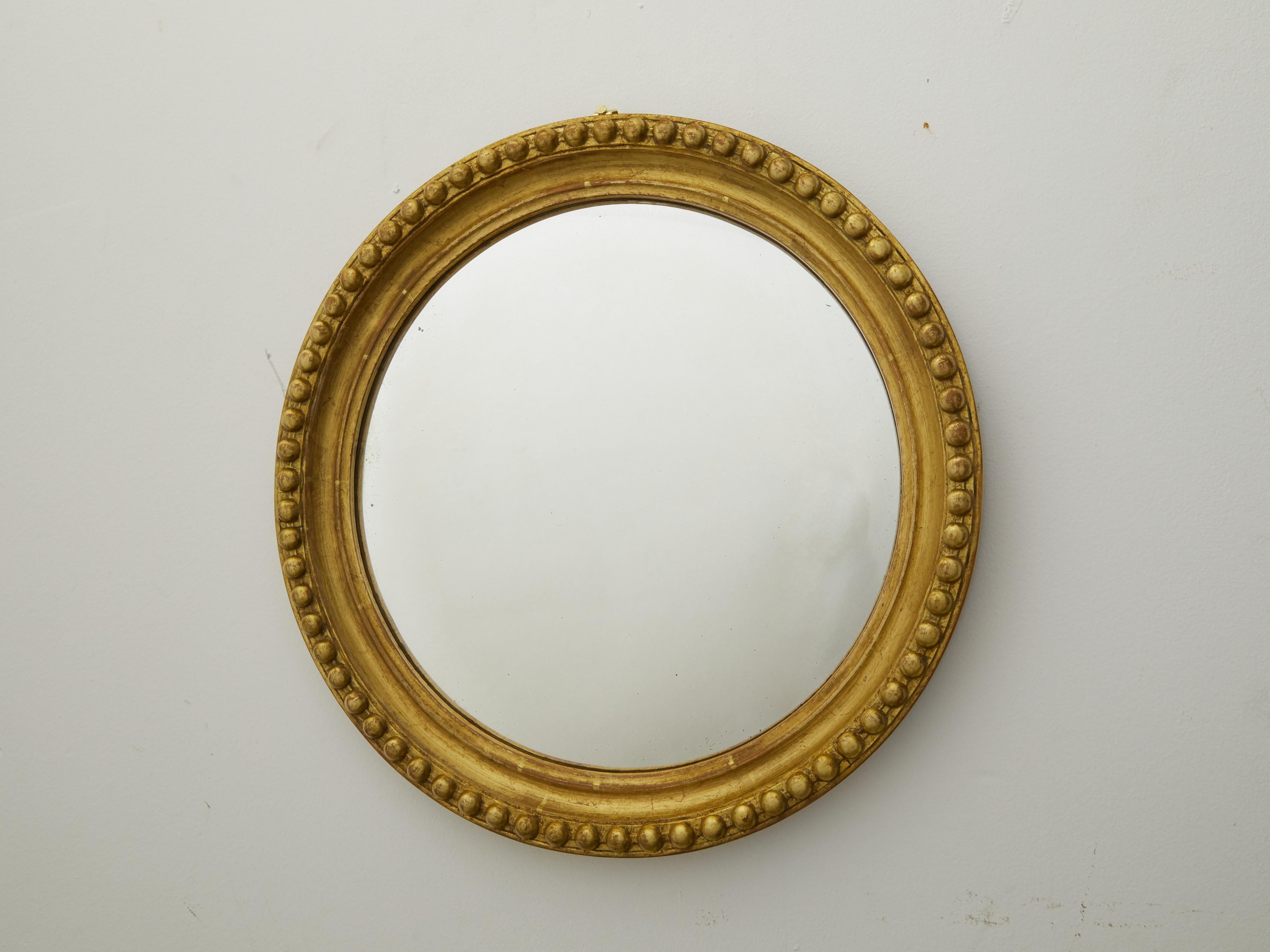 An English vintage giltwood convex mirror from the mid 20th century, with bead motifs. Created in England during the midcentury period, this mirror features a circular giltwood frame adorned with large beaded motifs, surrounding a convex mirror