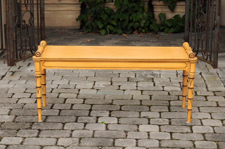 An English vintage painted wooden bench from the mid-20th century, with cylindrical armrests and faux bamboo legs. Born in England during the midcentury period, this exquisite painted bench attracts all of our attention with its goldenrod color with