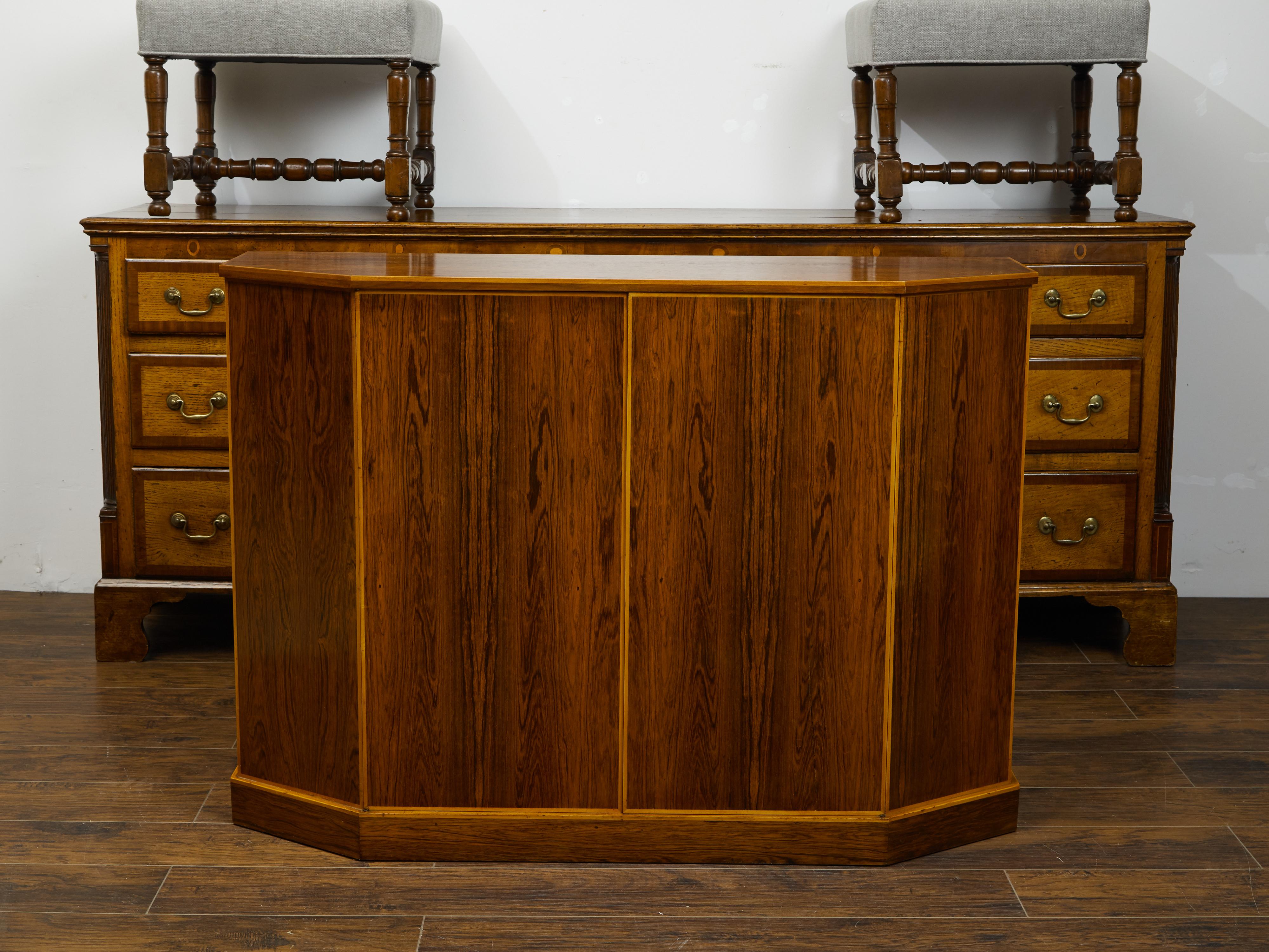 An English vintage rosewood credenza from the mid 20th century, with canted panels. Created in England during the midcentury period, this rosewood credenza features a polygonal top sitting above two doors flanked with canted sides. These doors open