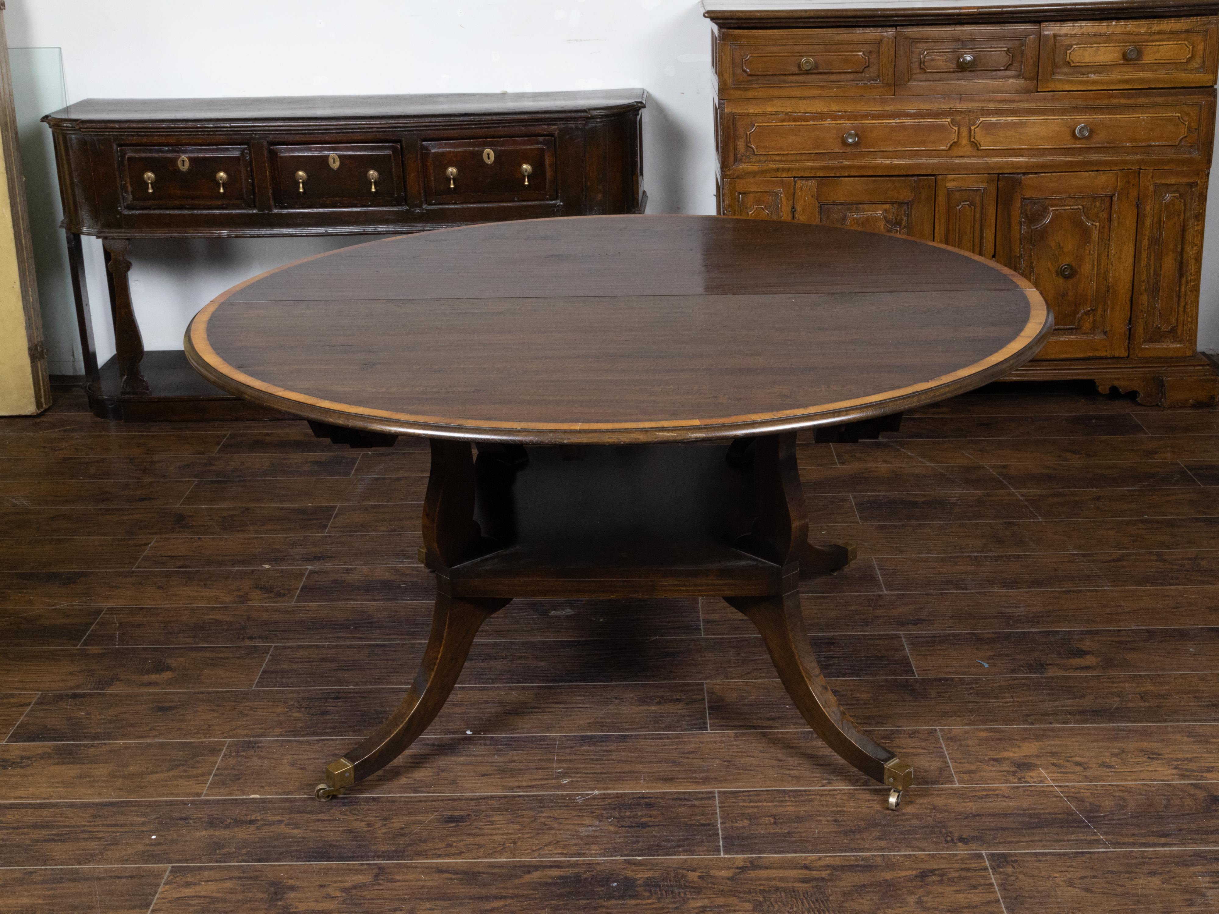 An English vintage oak dining or conference table from the Mid-20th Century with circular top, banding, two leaves extending it to an oval table, four legs and brass casters. Created in England during the midcentury period, this versatile table