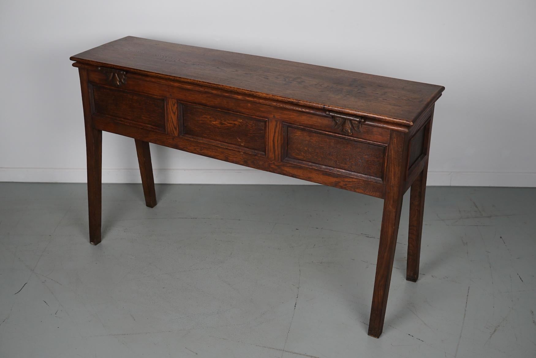 This elegant table was made in England. The table was made in solid oak with a beautiful grain pattern. It has a warm color with deep gloss. It was originally a payment table and later in it's life converted into this side table with storage.