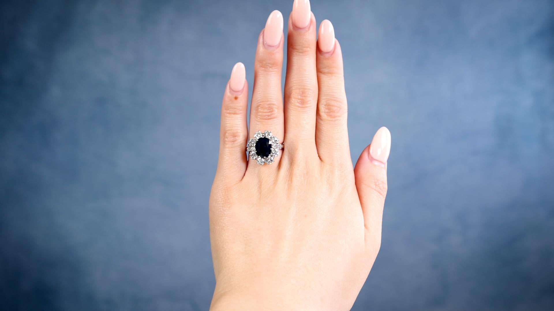 Ein Vintage English Sapphire Diamond 18k White Gold Cluster Ring. Mit einem ovalen Saphir im Mischschliff mit einem Gewicht von etwa 2.50 Karat. Akzentuiert durch zwei spitz zulaufende Baguette-Diamanten und acht runde Diamanten im Brillantschliff