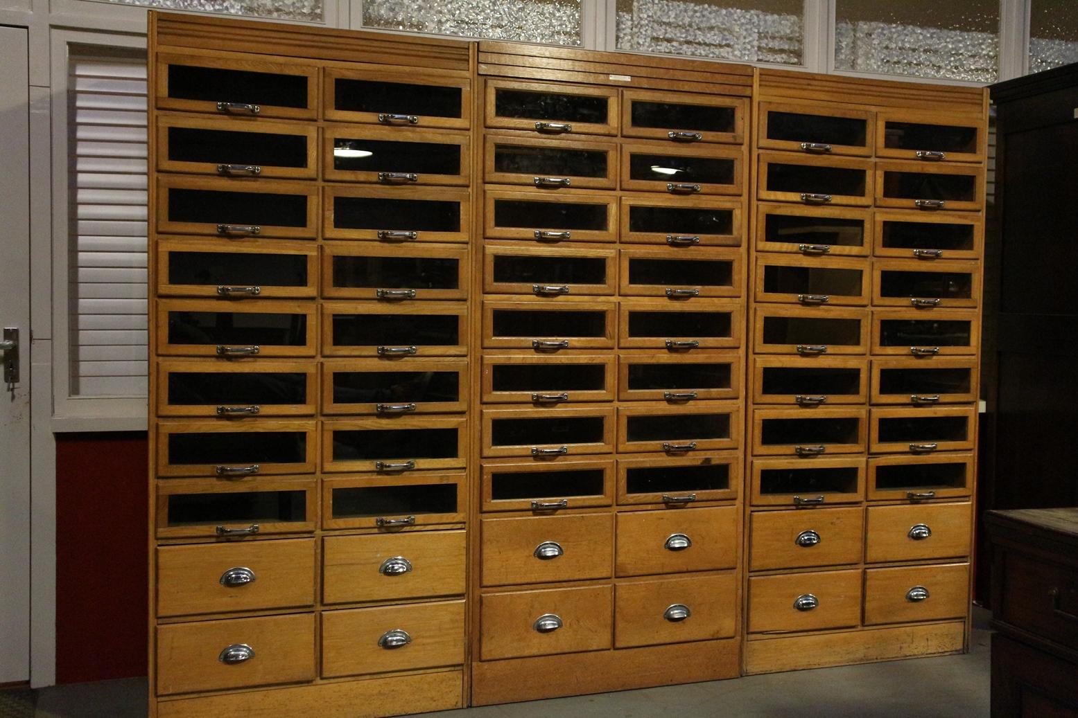 Beautiful three old shop showcases made of beech wood in light color. The middle is not exactly the same as the other two cabinets but fit well together. Also for sale separately. 48 drawers with glass front and 12 closed drawers
Origin: