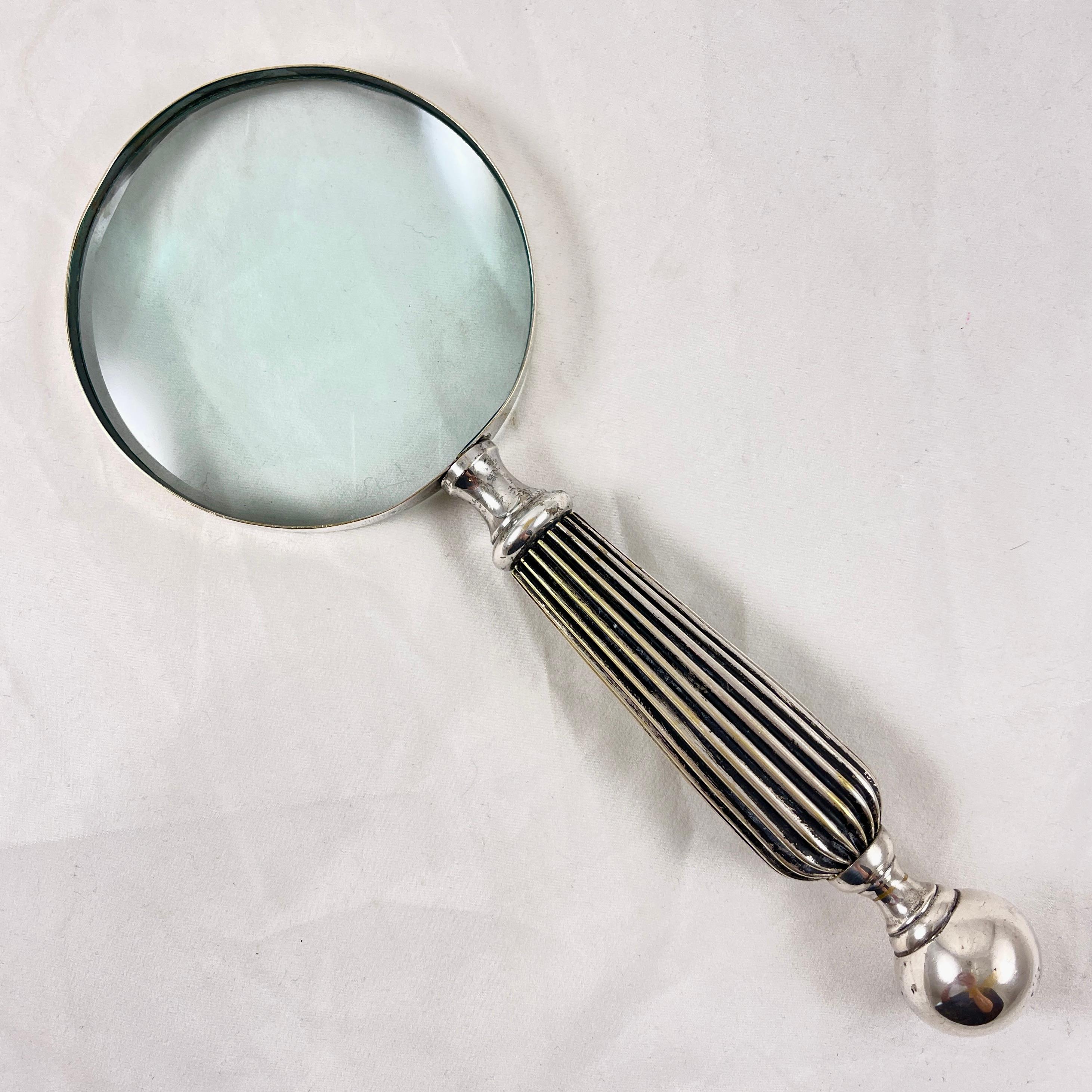 A substantial, silver plated hand-held magnifying glass, circa 1980s.

Perfect for the desk top or a library, this heavy magnifying has a ribbed metal handle terminating in a solid ball. Securely attached to a silver rimmed round glass.

10 in. L x