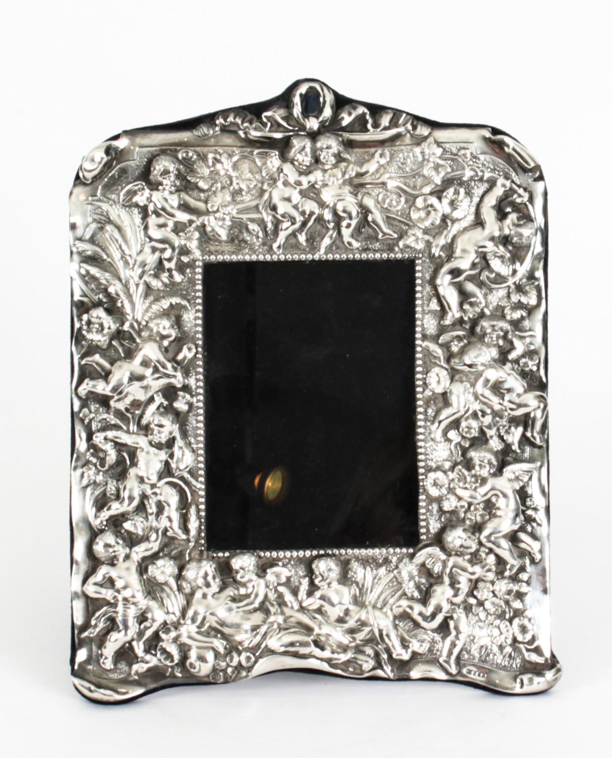 A truly superb vintage sterling silver photo frame with hallmarks and the makers mark of Neil Lasher Silverware, London and dated 1995.

The beautiful rectangular photo frame is superbly decorated with ribbons, flowers and winged cherubs in high