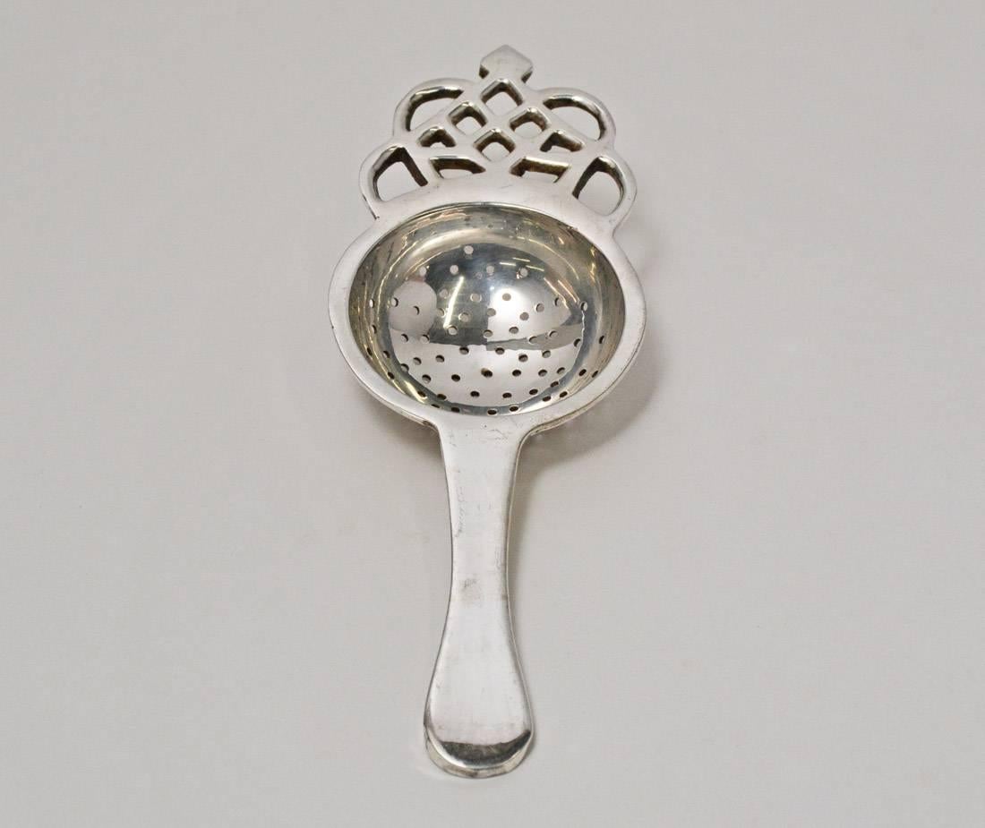 The vintage silver-metal strainer for loose tea is in the English style of the 18th century topped with filigree design.