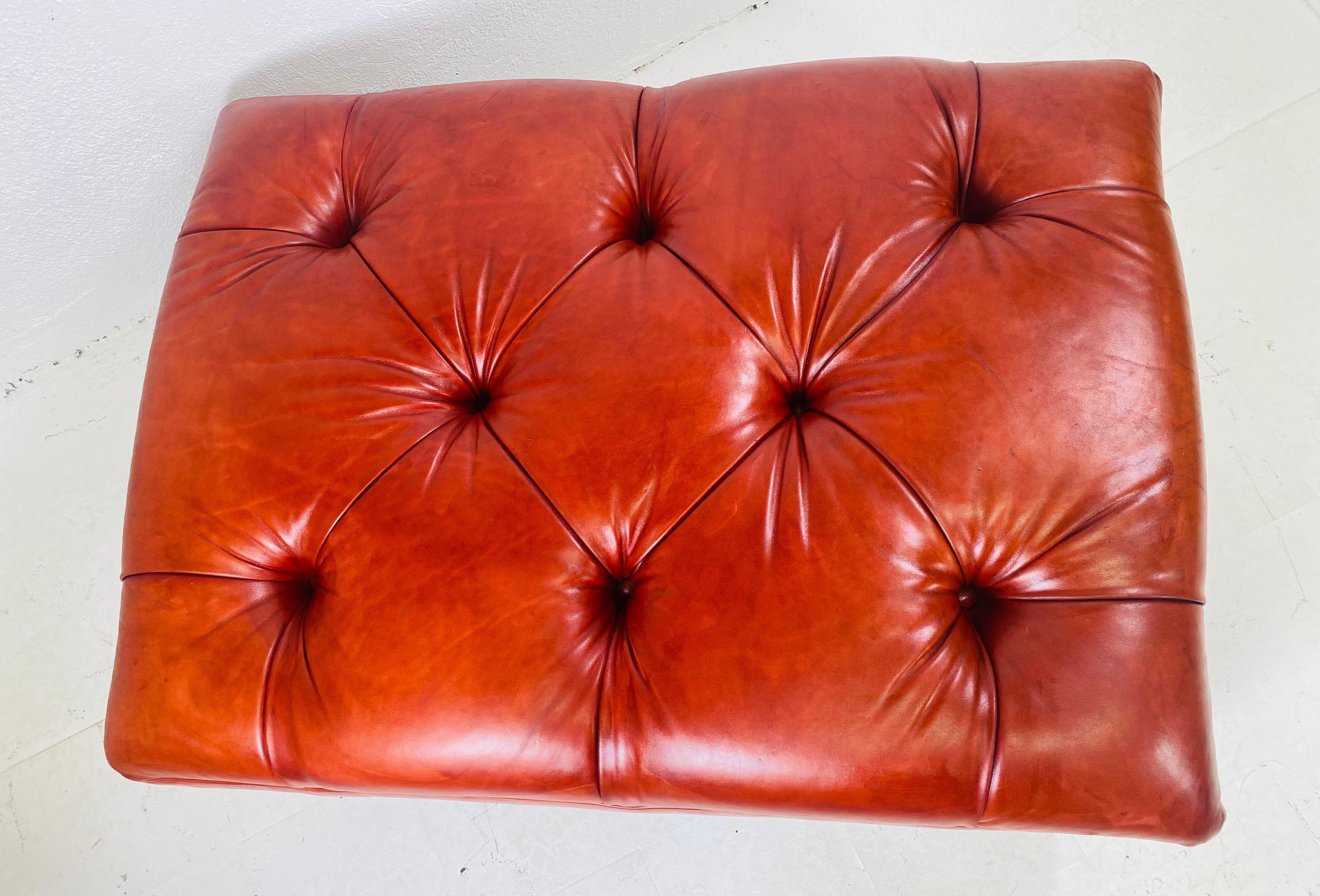 This is a vintage English traditional style tufted ottoman. This ottoman stands on four bun feet with casters and has a beautiful amber rust weathered leather.