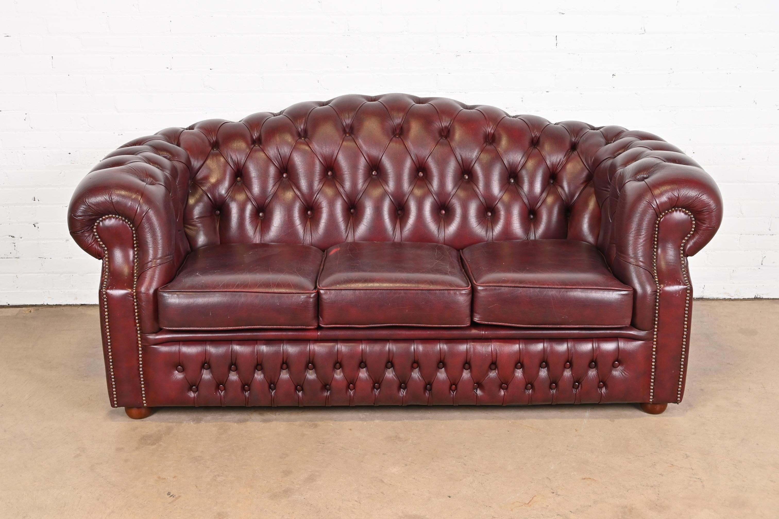 A gorgeous vintage camelback Chesterfield sofa

England, Circa Late 20th Century

Tufted oxblood leather, with brass studs and mahogany bun feet.

Measures: 76
