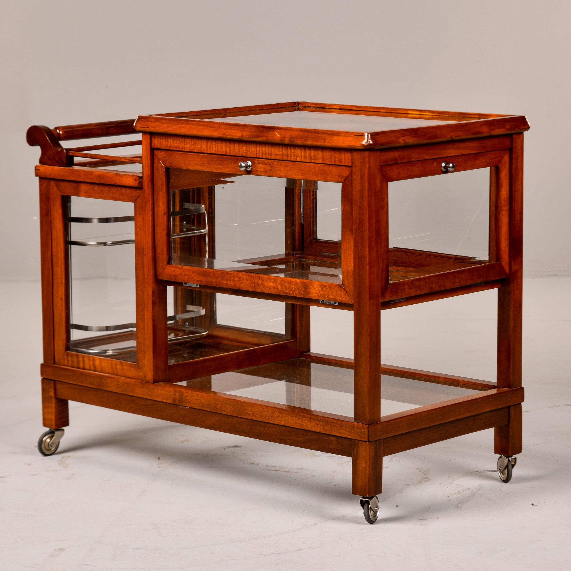 Found in England, this walnut and glass bar cart or trolley dates from the 1940s. Section with bottle rack and wood handle at the top has a locking glass door that opens. Top section of the taller part of the cart opens with drop down doors on both