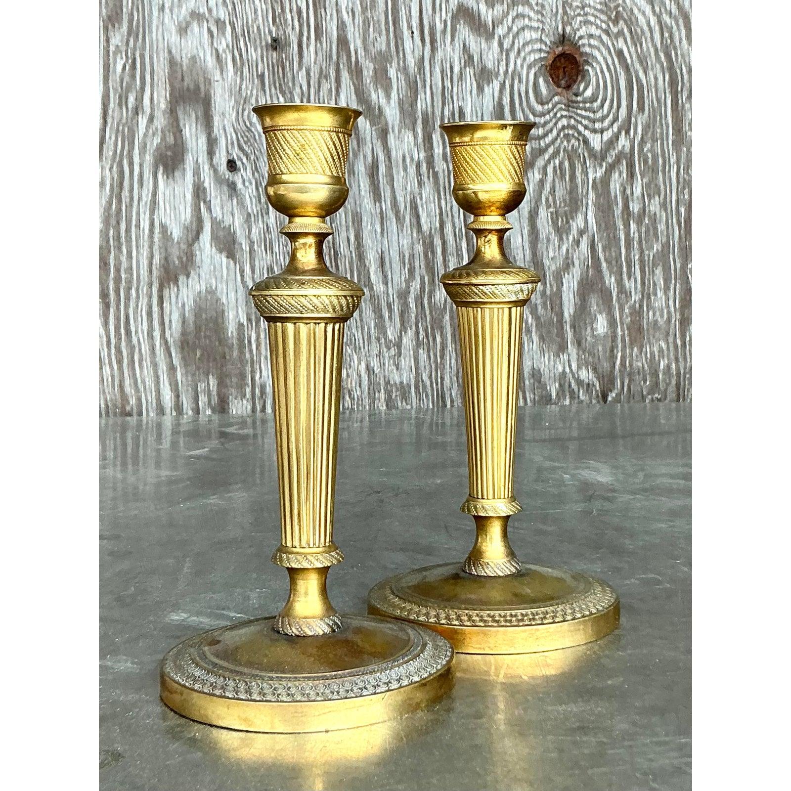 Eleva il tuo arredamento con questa squisita coppia di candelieri vintage in ottone inciso. Questi pezzi senza tempo mostrano intricate colonne scanalate e delicati dettagli incisi, catturando la raffinata eleganza del design neoclassico. La calda